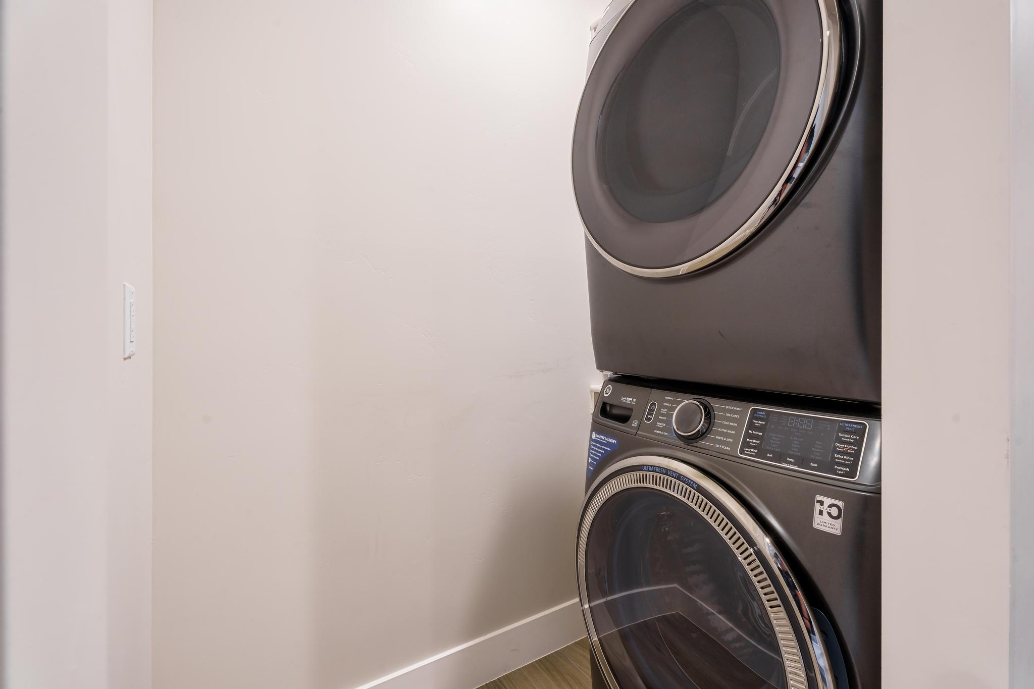 Stackable front-loading washer and dryer unit with dark finishes and chrome accents