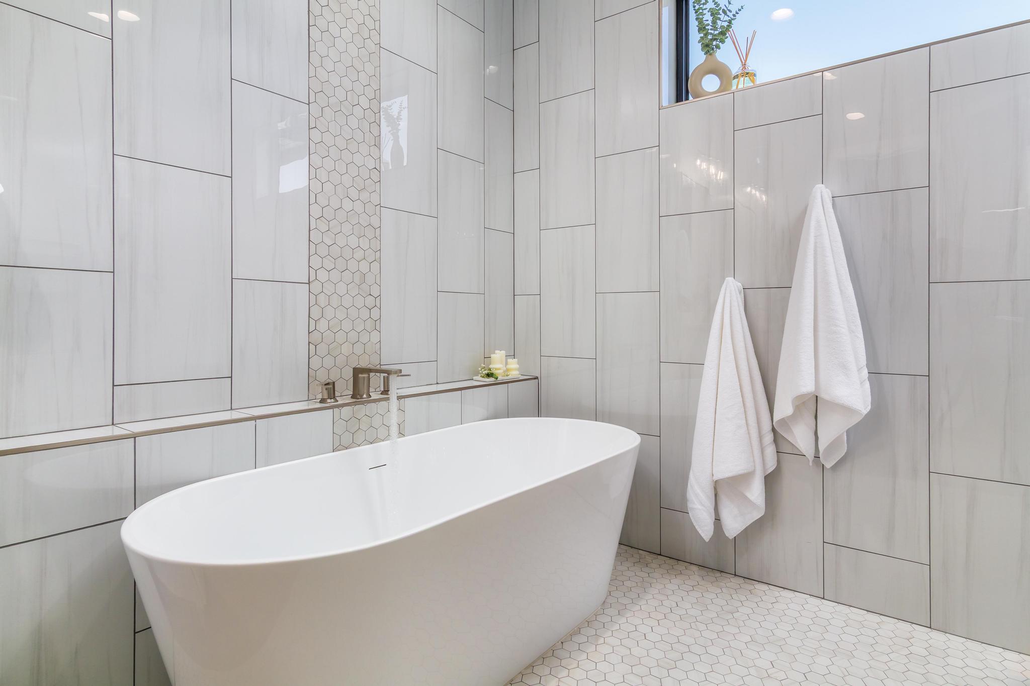 Freestanding soaking tub with a floor-mounted brushed nickel faucet, set against a tiled wall featuring rectangular and hexagonal patterns