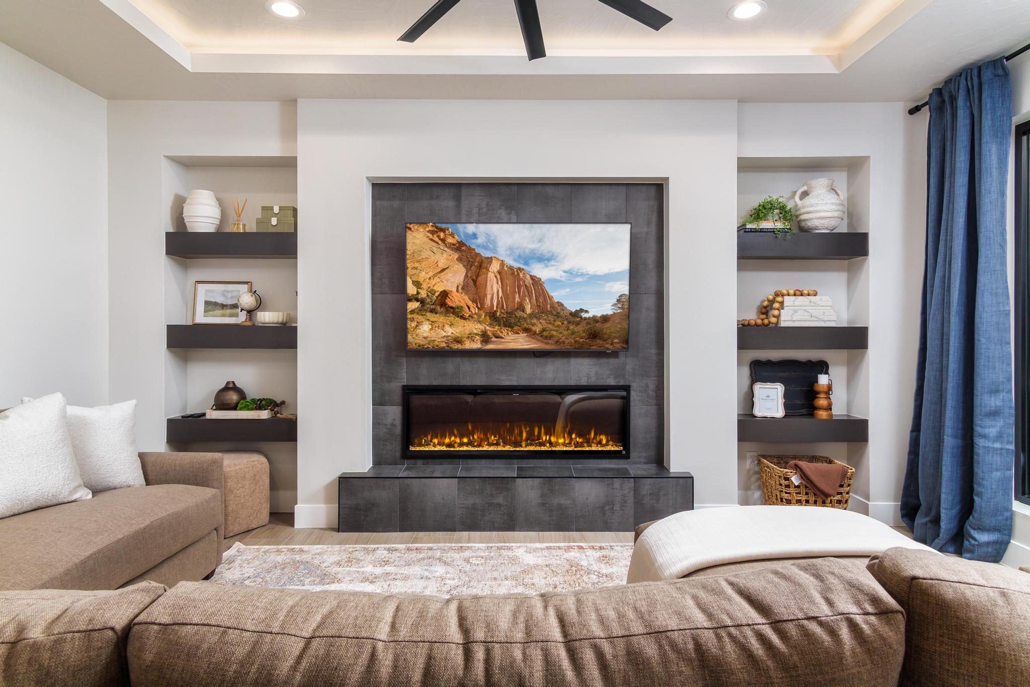 Integrated entertainment wall featuring an electric fireplace with a dark tile surround, recessed television alcove, and built-in shelving