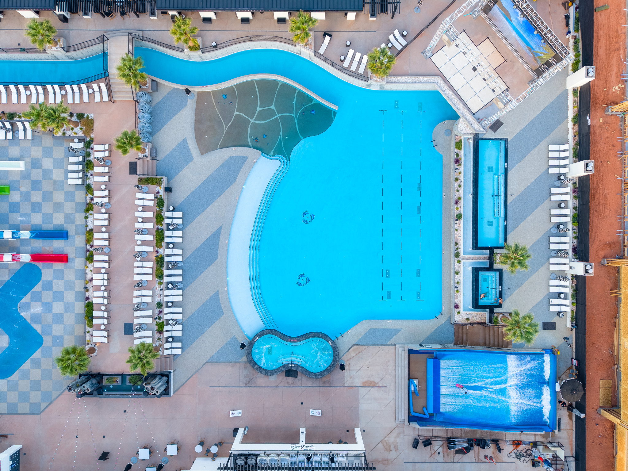 Expansive aquatic area featuring a large swimming pool, a lazy river, two additional rectangular pools, two circular spas, and a surf simulator