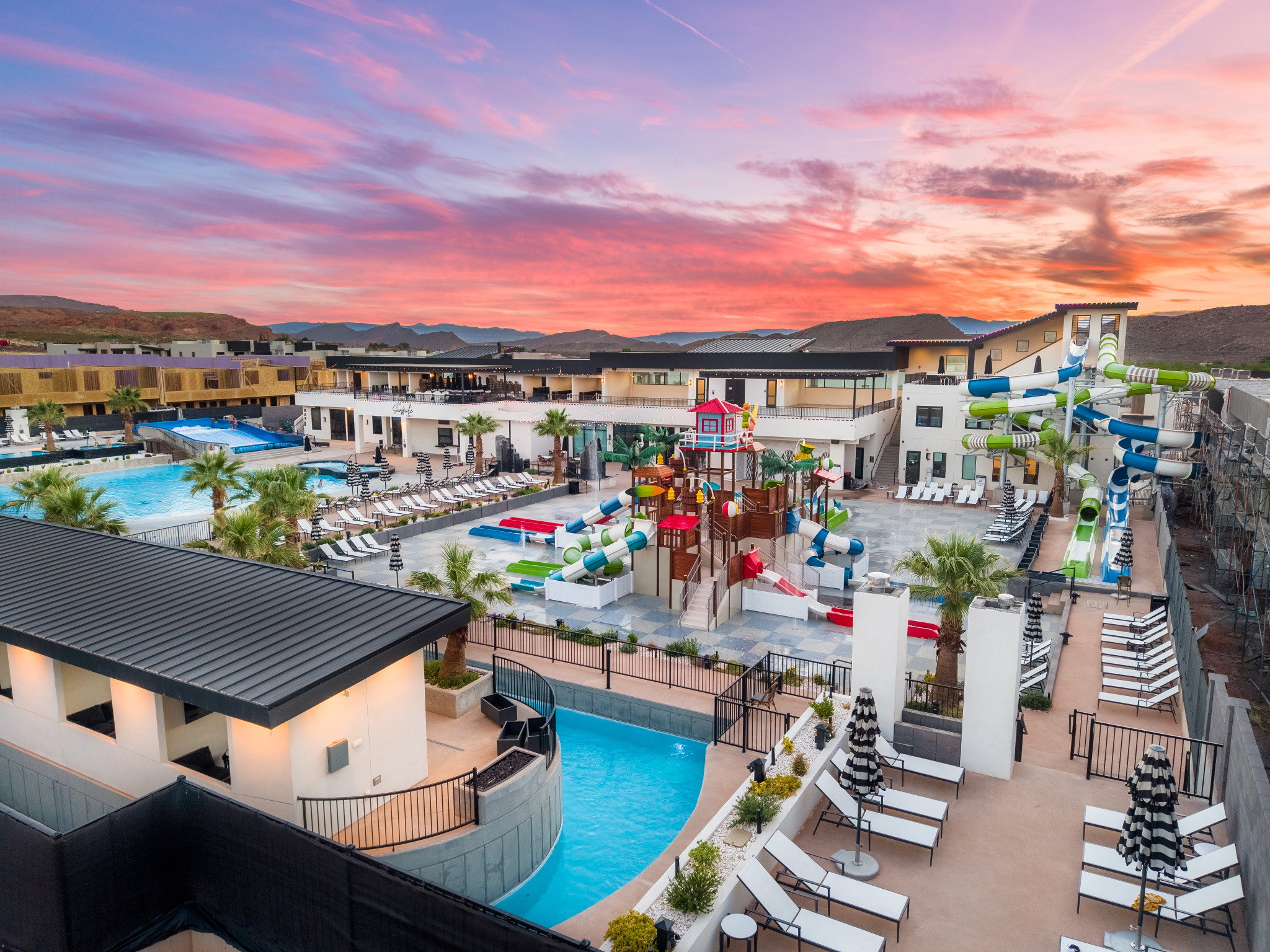 Extensive outdoor recreation area featuring multiple pools, vibrant water slides, a dedicated children's play structure, and numerous lounge seating options