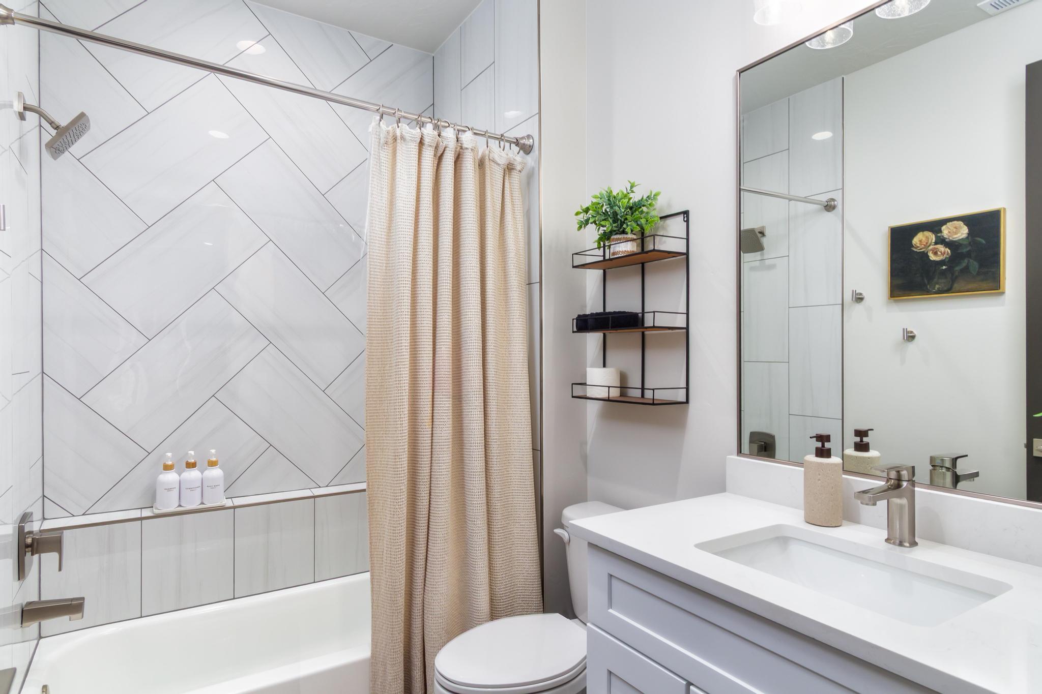 Bathroom featuring a white subway tile shower surround with a herringbone pattern, a built-in shower niche, a white tub, and a vanity with a white countertop and integrated rectangular sink