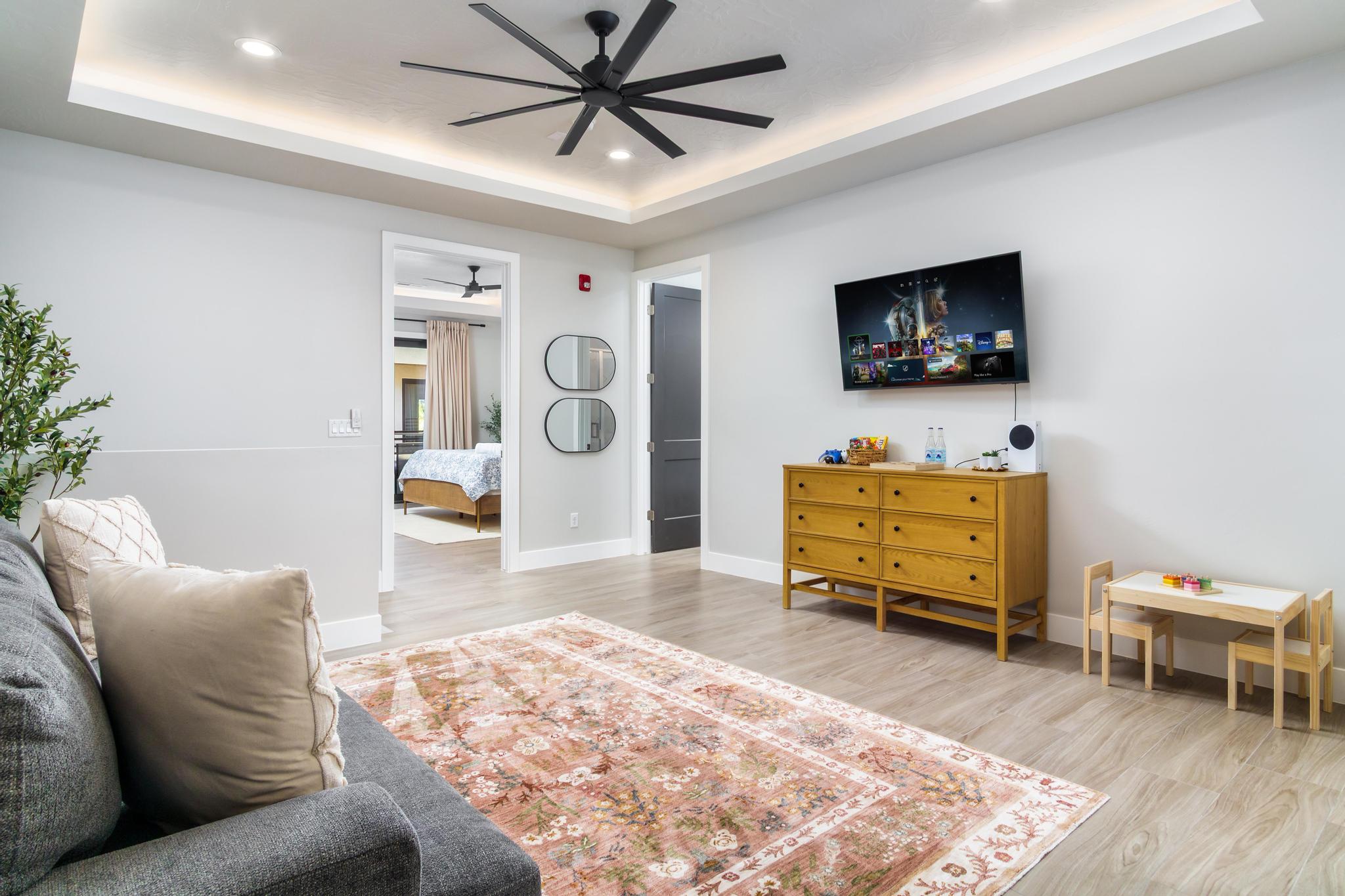 Spacious room featuring wood-finish flooring, a recessed ceiling with integrated lighting, and a modern ceiling fan