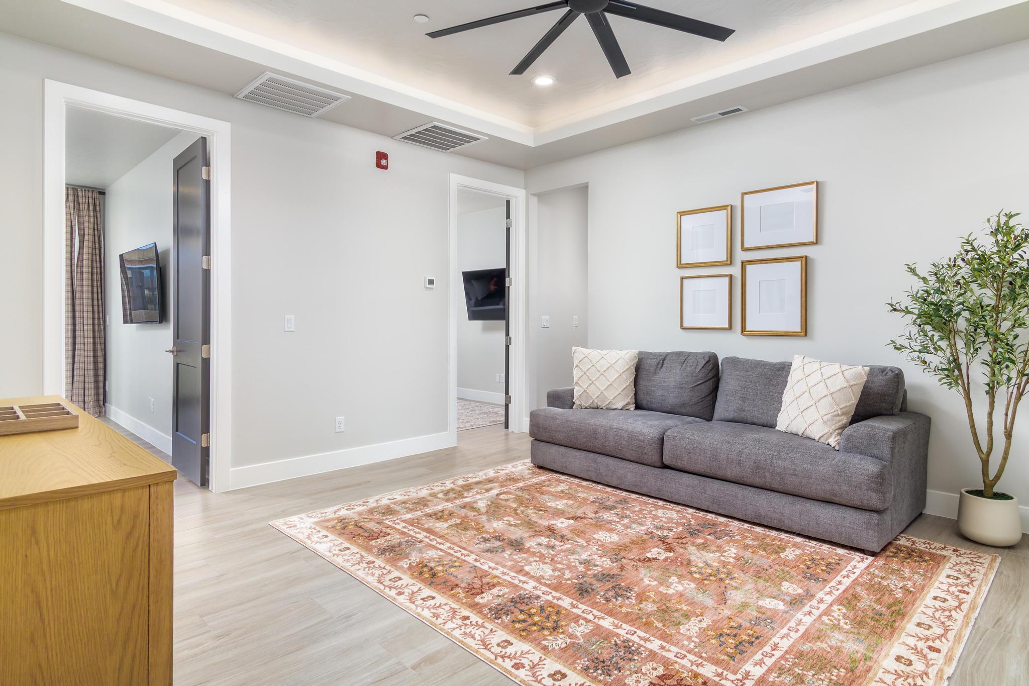 Recessed ceiling with a modern black ceiling fan, light wood-finish flooring, and white baseboards