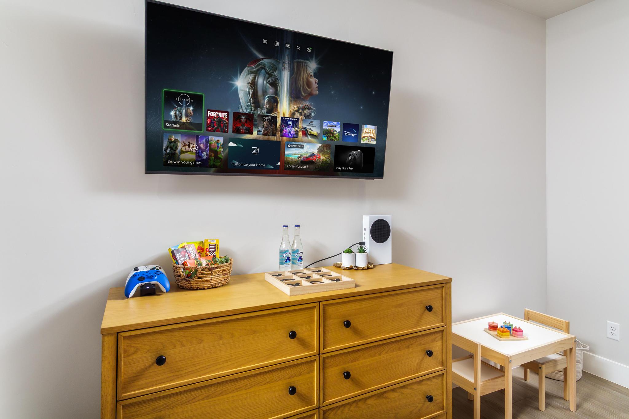 Wall-mounted television above a light wood-finish dresser with black knob hardware