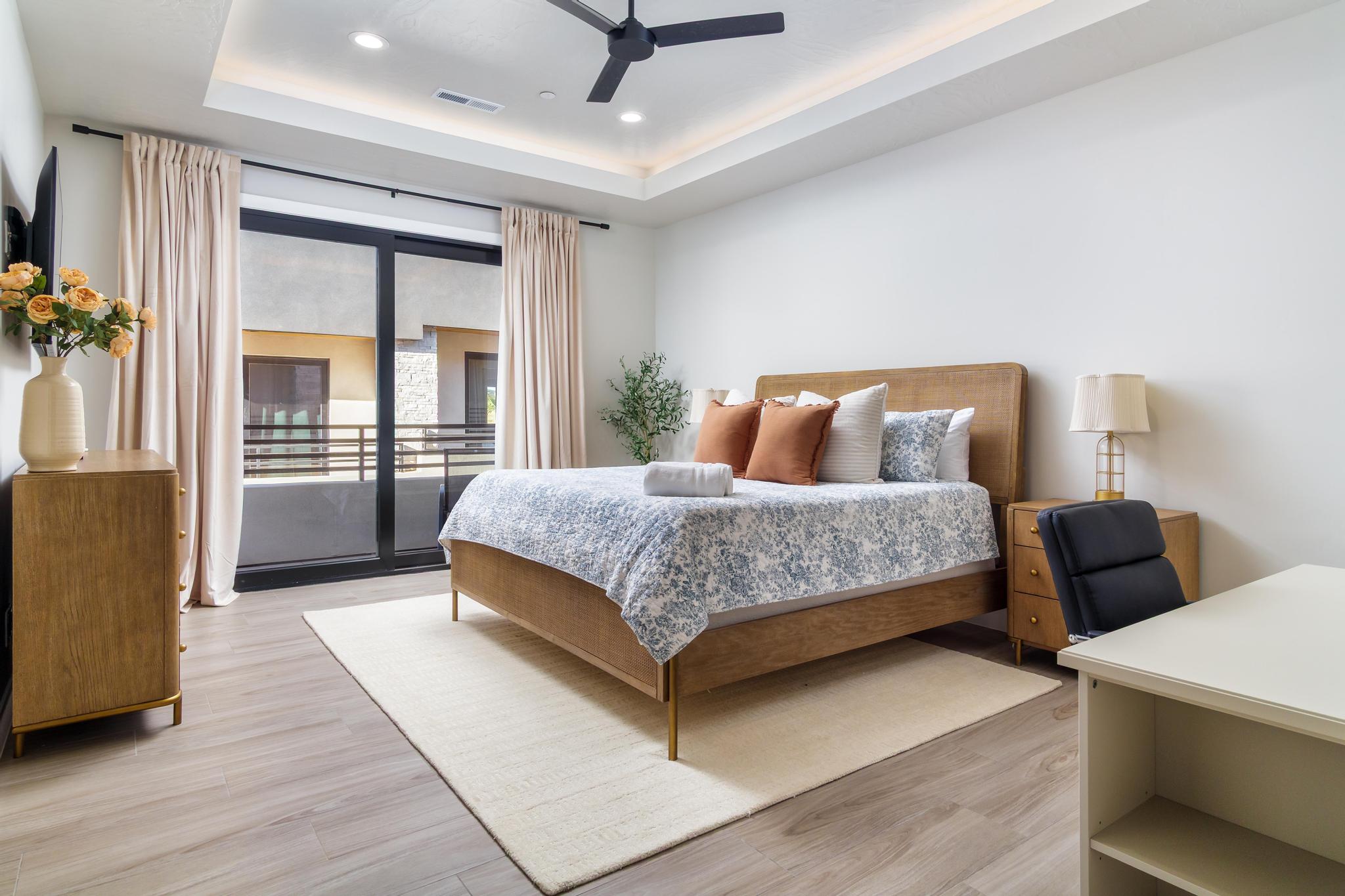 Bedroom featuring wood-finish flooring, a tray ceiling with recessed lighting, a ceiling fan, and sliding glass doors opening to a balcony with metal railings