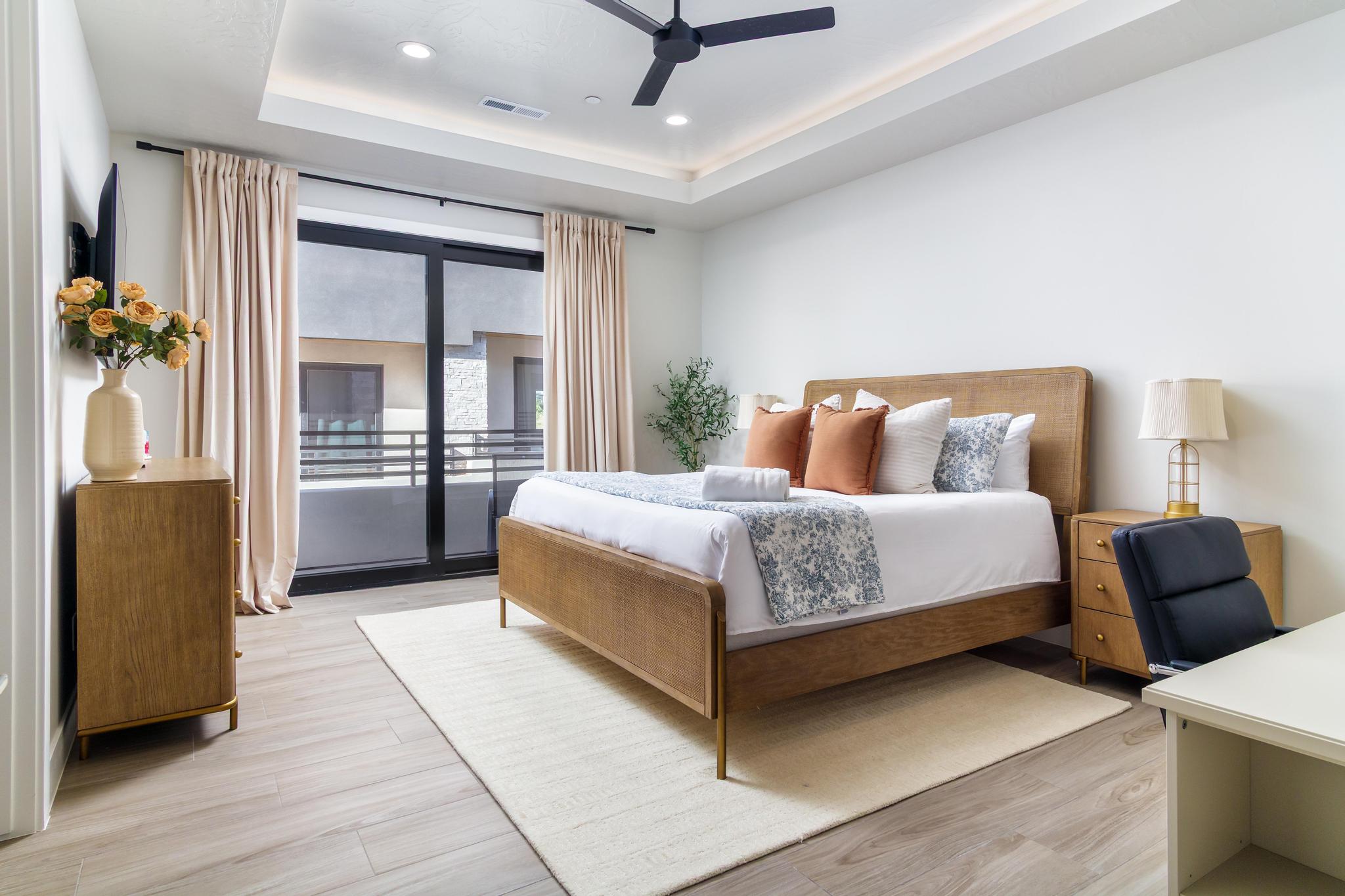 Spacious room featuring light wood-finish flooring, a tray ceiling with recessed lighting, a ceiling fan, and large sliding glass doors opening to an exterior balcony