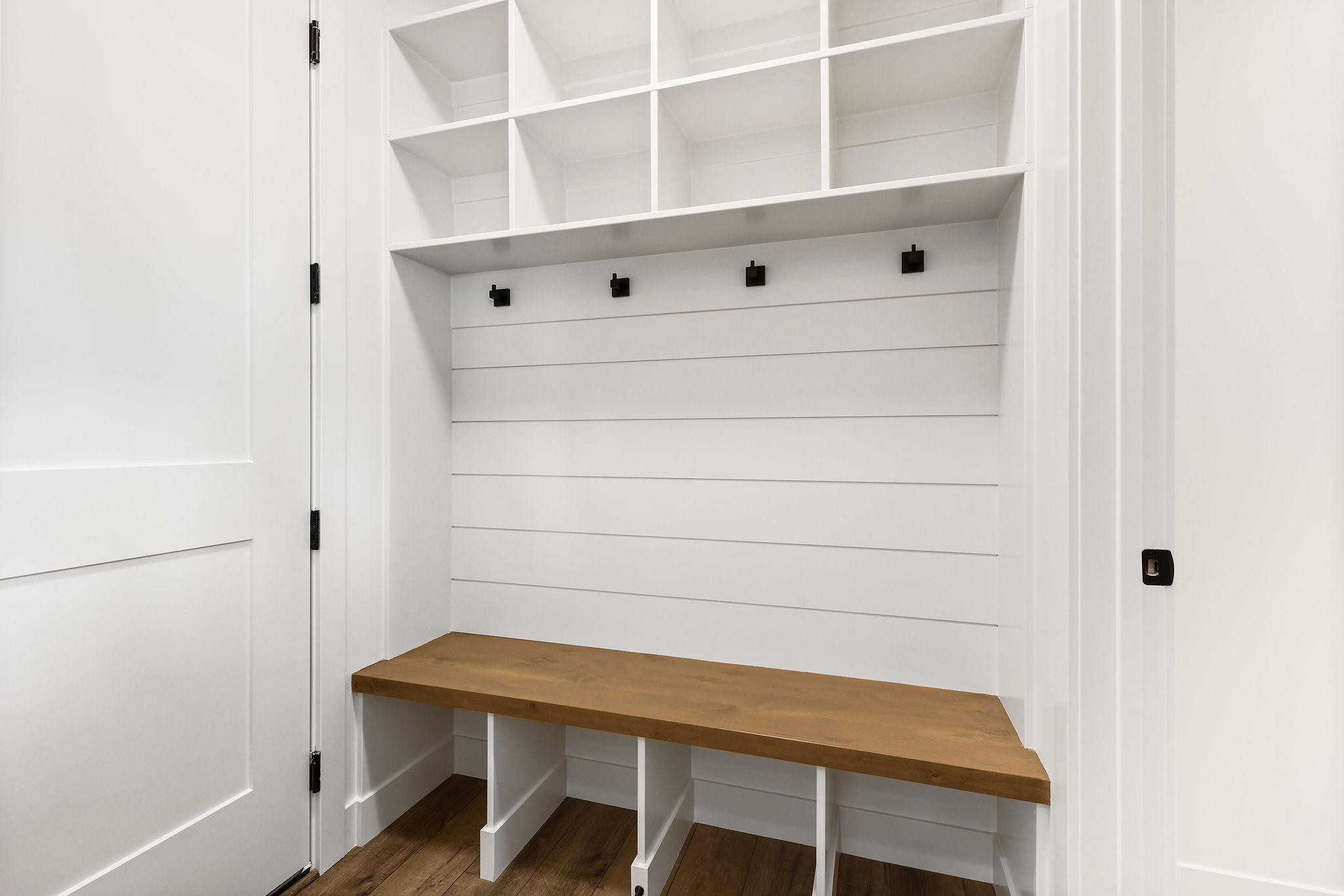 Built-in entryway storage with a natural wood-finish bench, white shiplap paneling, and matte black coat hooks