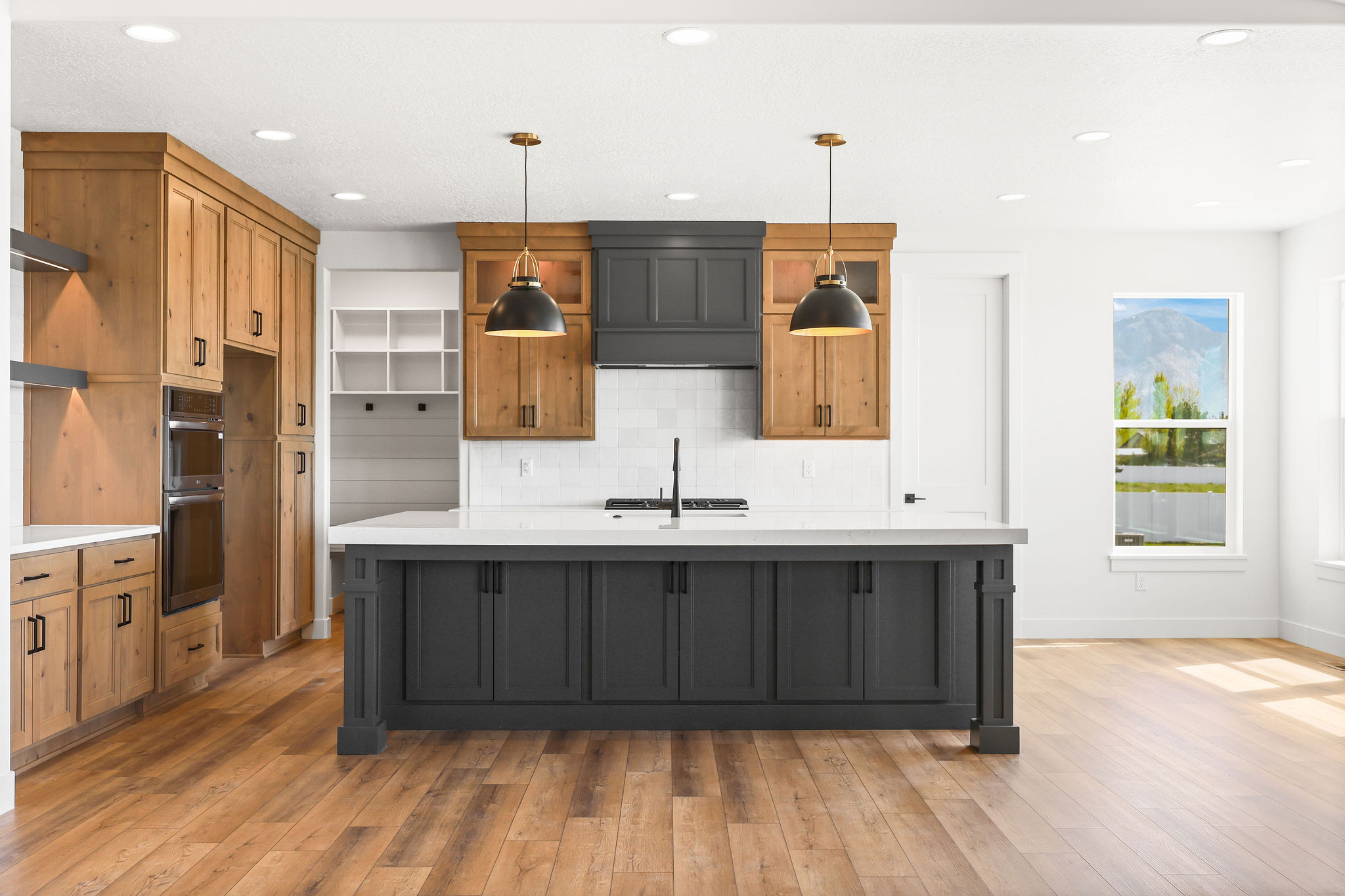 Spacious kitchen featuring a large central island with dark cabinetry and a light-toned countertop, wood-finish flooring, and recessed ceiling lights