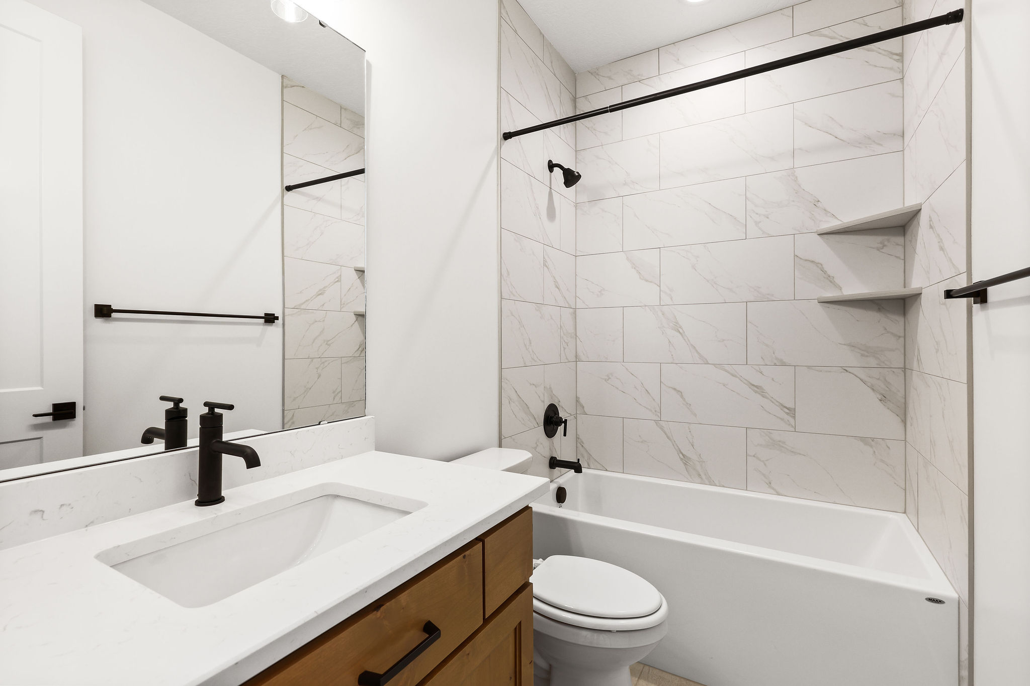 Bathroom featuring a wood-finish vanity with a white countertop and integrated sink, matte black faucet, and a large mirror