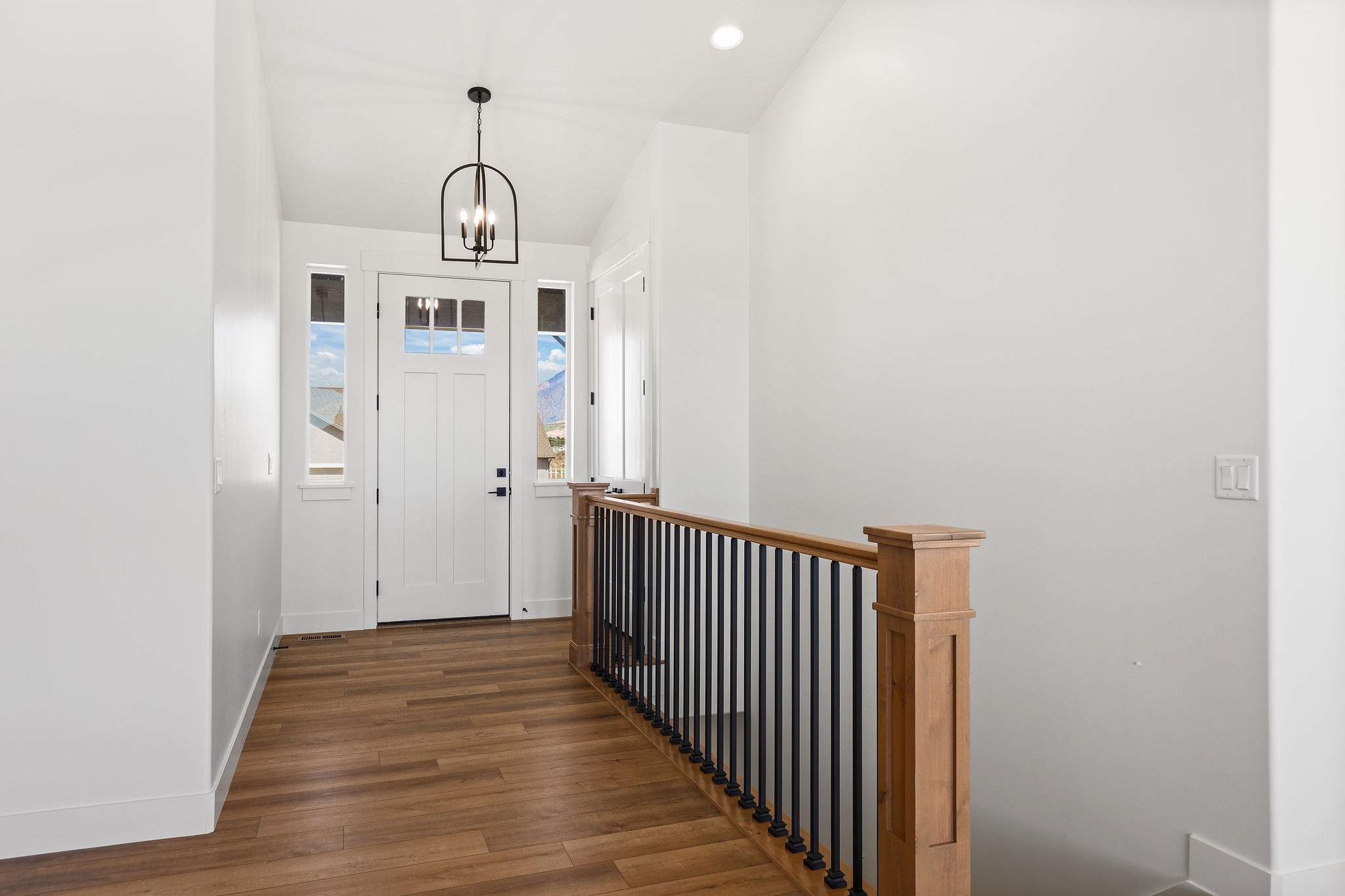 Foyer featuring wood-finish flooring, a white paneled entry door with clear glass panels, side light windows, and an overhead black metal chandelier