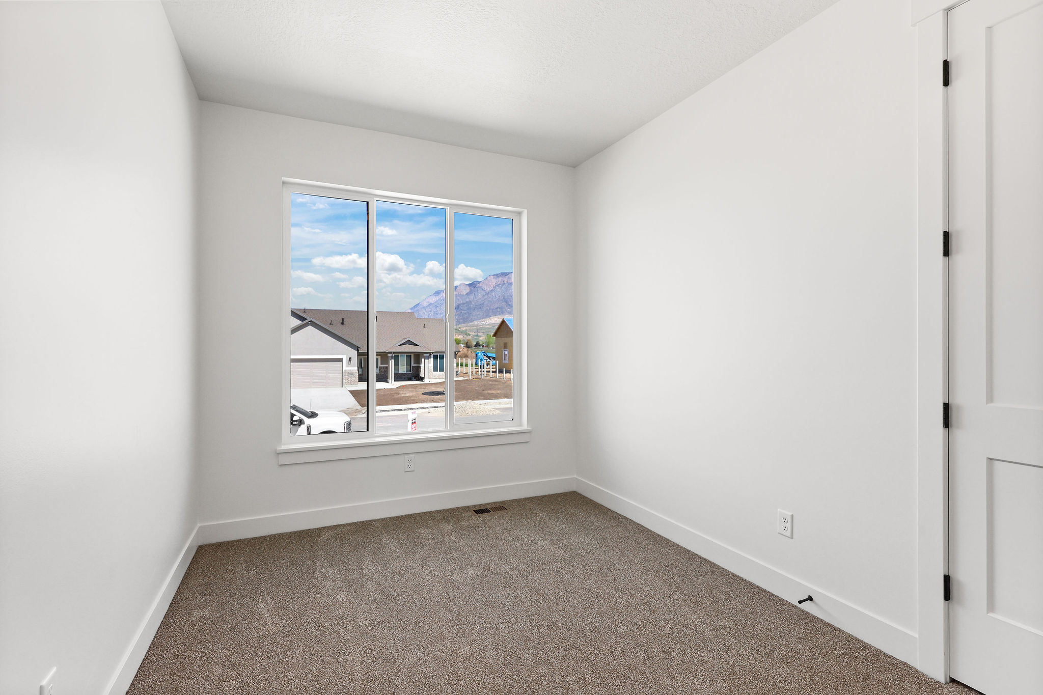 Carpeted room with a large window, white walls, and a white door with black hinges