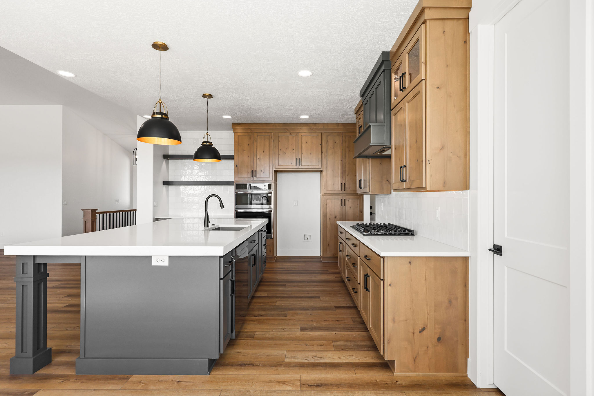 Spacious kitchen featuring a large island with a white countertop, two-tone cabinetry, wood-finish flooring, a gas range, and a subway tile backsplash