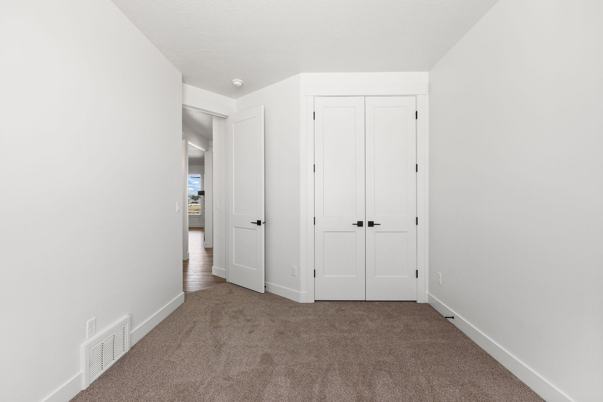 Carpeted room with white walls, baseboards, and two-panel interior doors with matte black hardware
