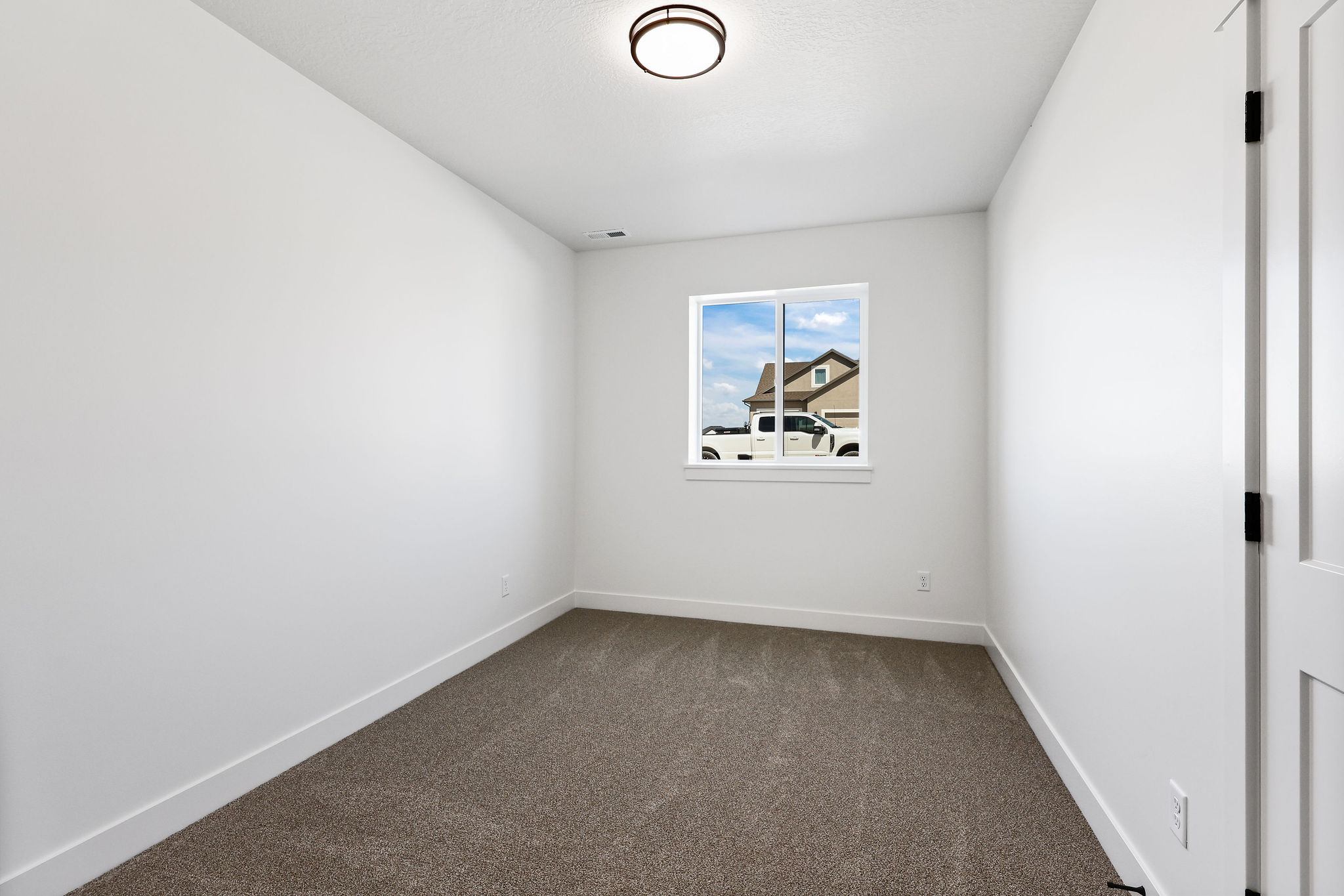 Bright room featuring a window with exterior views, neutral carpeting, white walls, and a contemporary flush-mount ceiling light