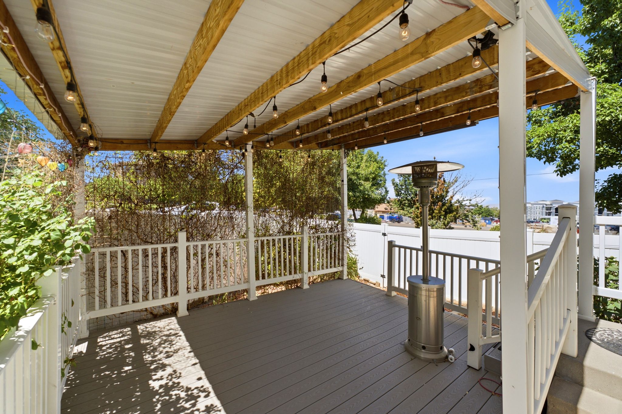 Covered outdoor deck featuring composite decking, white railing, exposed wood beams, and a corrugated metal ceiling