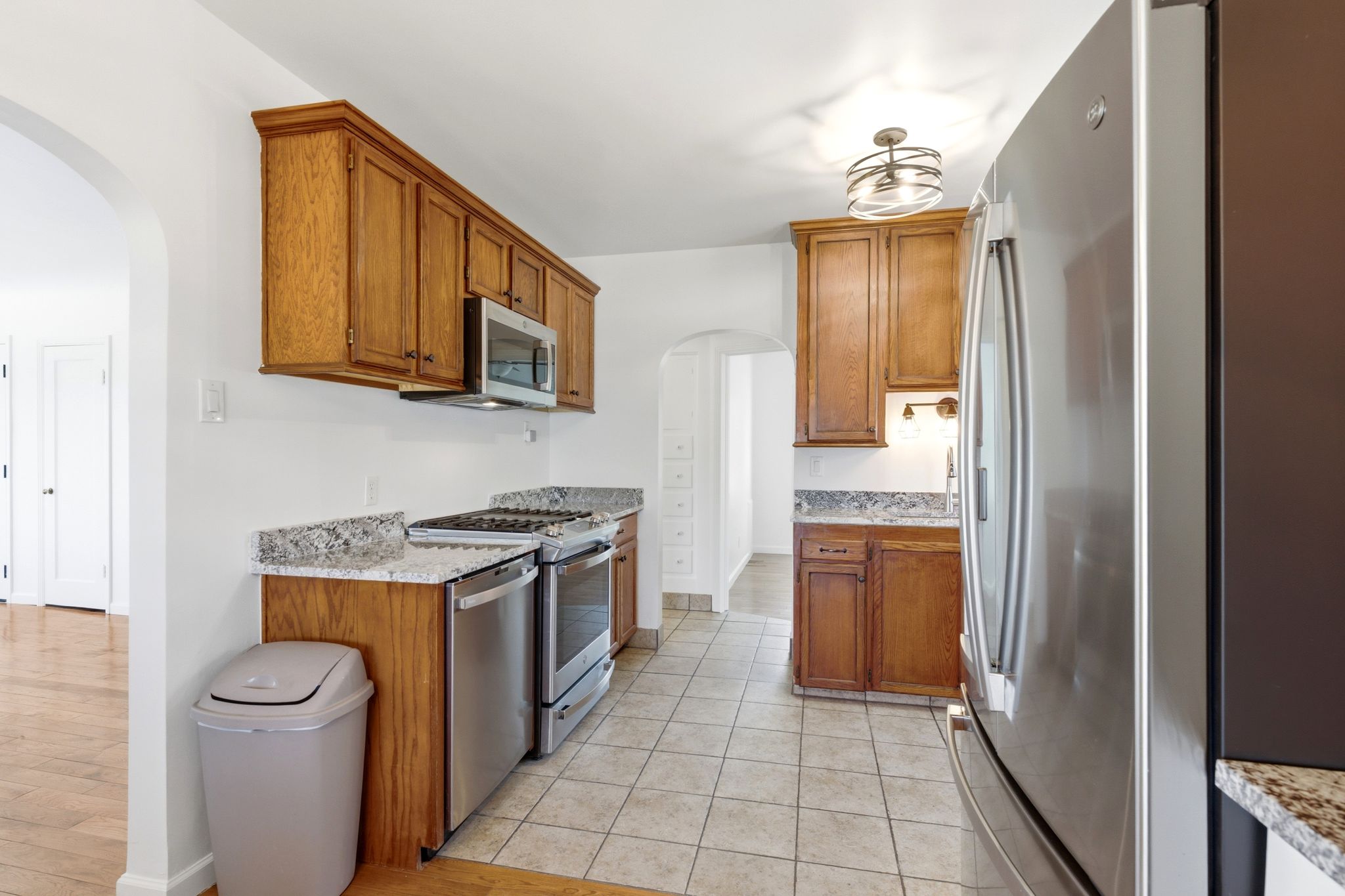 Kitchen featuring wood cabinetry, stainless steel appliances, speckled stone countertops, and tile flooring