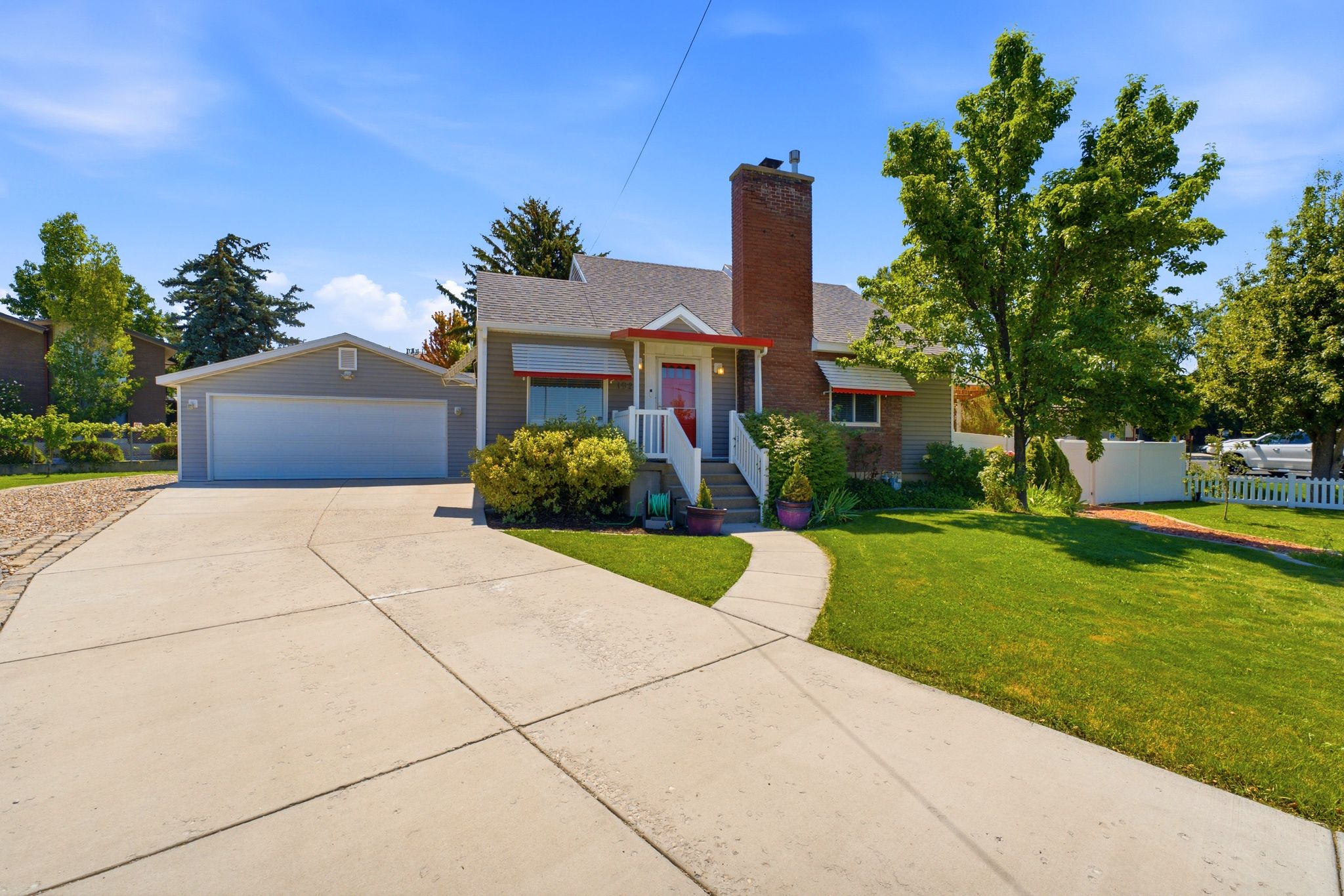 Exterior featuring a brick chimney, a two-car garage, a concrete driveway, a manicured lawn, and mature trees