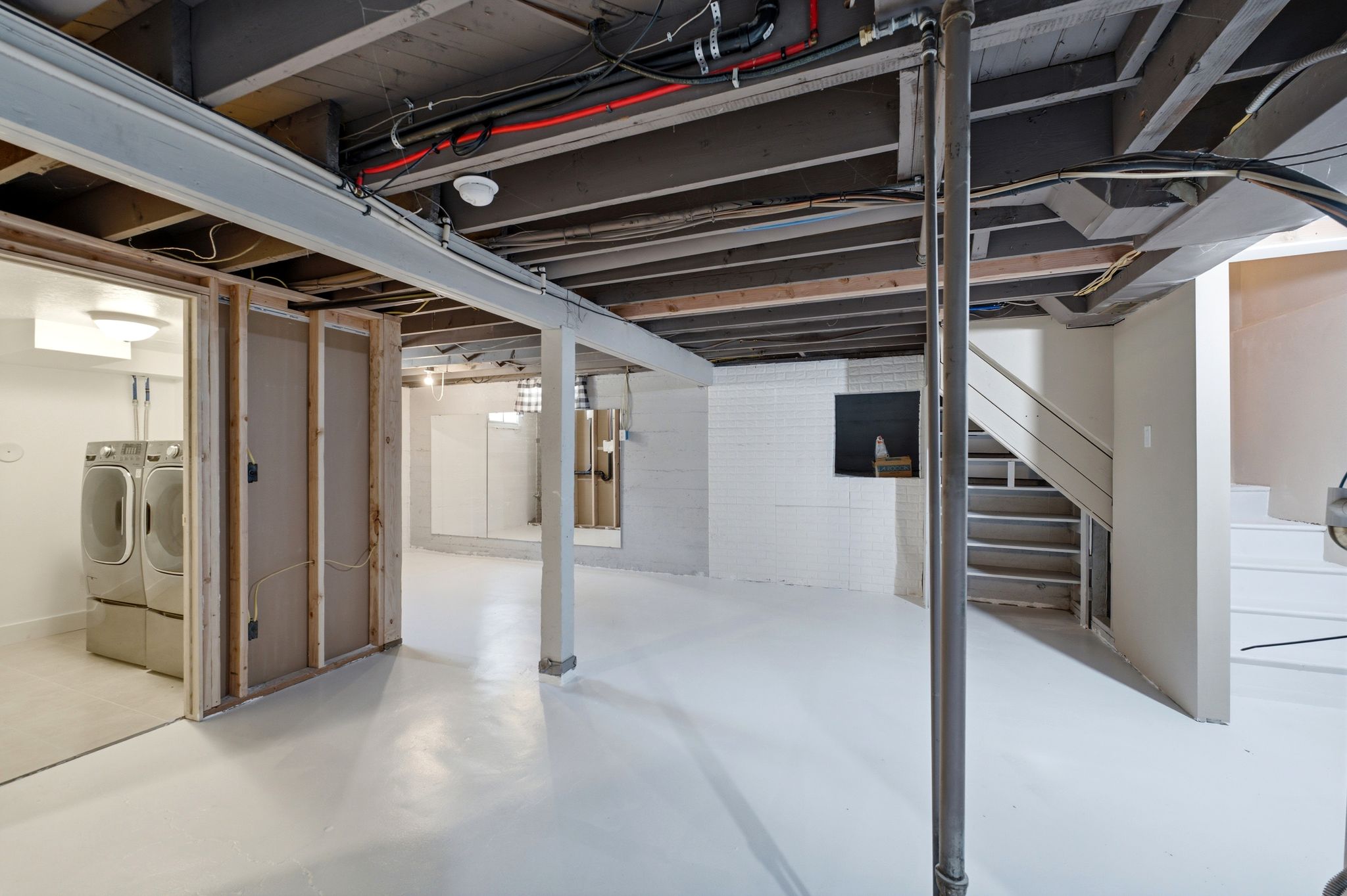 Unfinished basement space featuring exposed ceiling joists, white painted concrete flooring, and a laundry area with tile flooring
