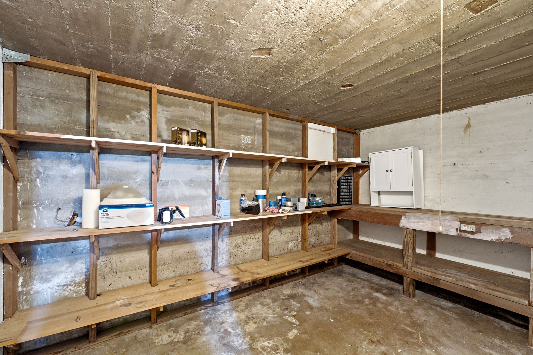 Utility space with concrete walls and ceiling, featuring built-in wooden shelving and a workbench