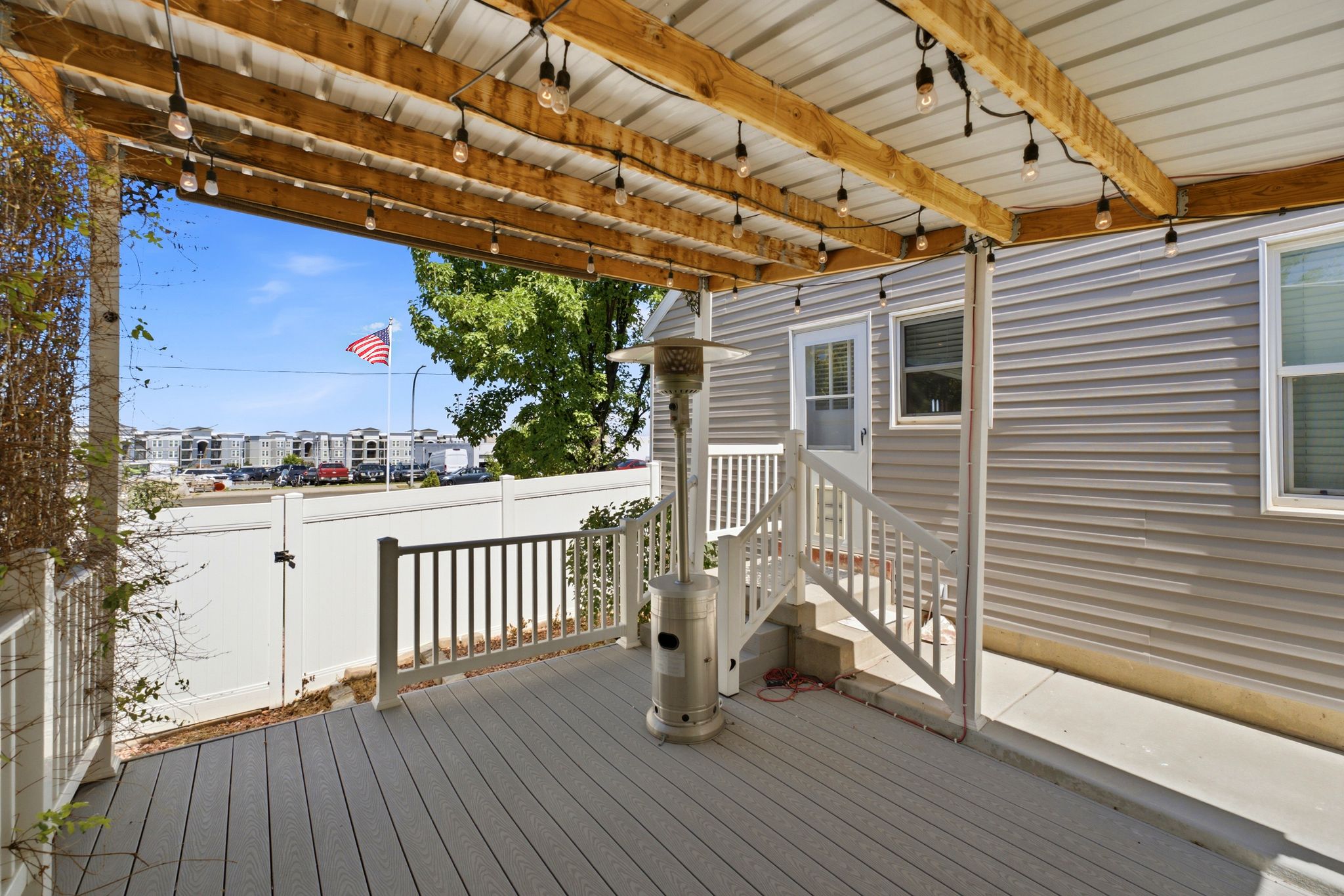 Covered outdoor deck featuring composite decking, white railings, and a wood-beamed ceiling with string lighting