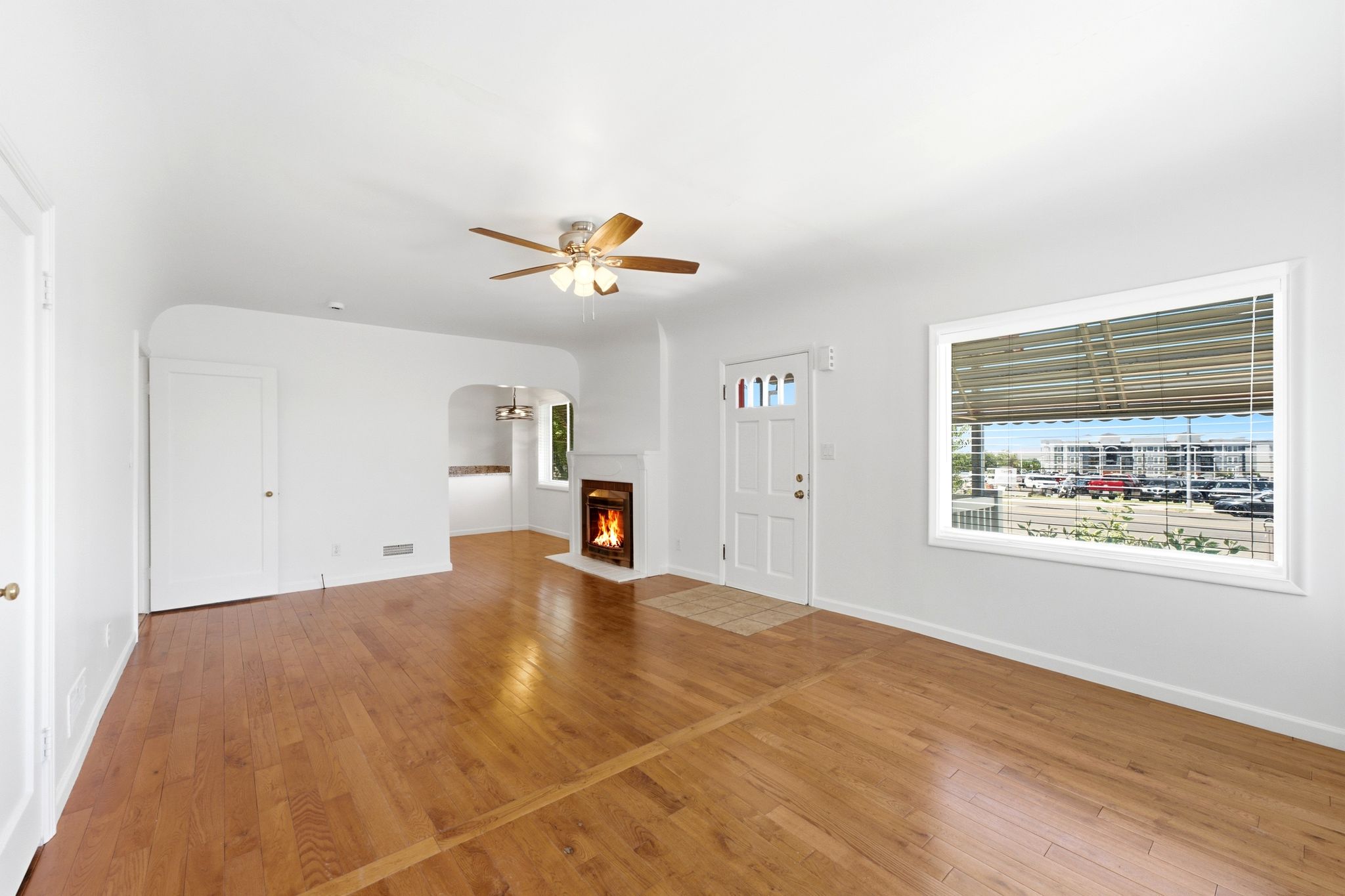 Living area featuring wood-finish flooring, a ceiling fan, a fireplace with a white mantel, and a front entry door with glass inserts