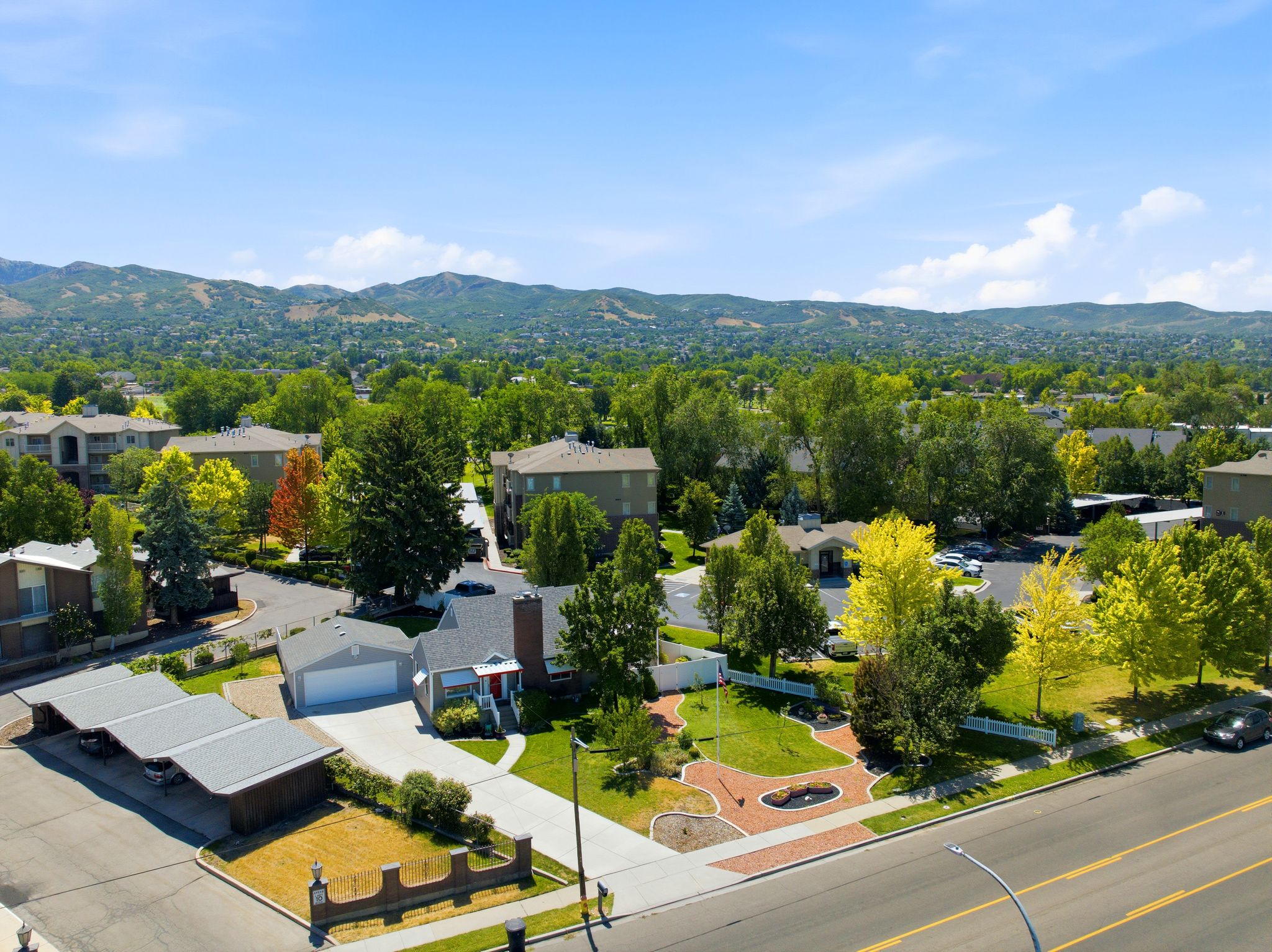 Aerial perspective showcasing a residential property with a detached garage, a landscaped front yard with brick-paved pathways, and mature trees