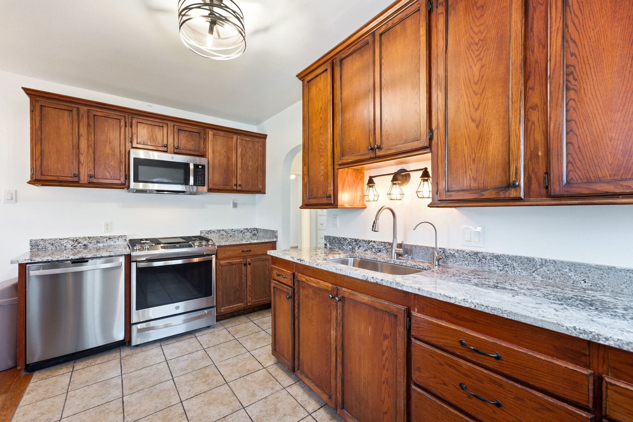 Kitchen featuring wood cabinetry, stainless steel appliances, granite countertops, and tiled flooring