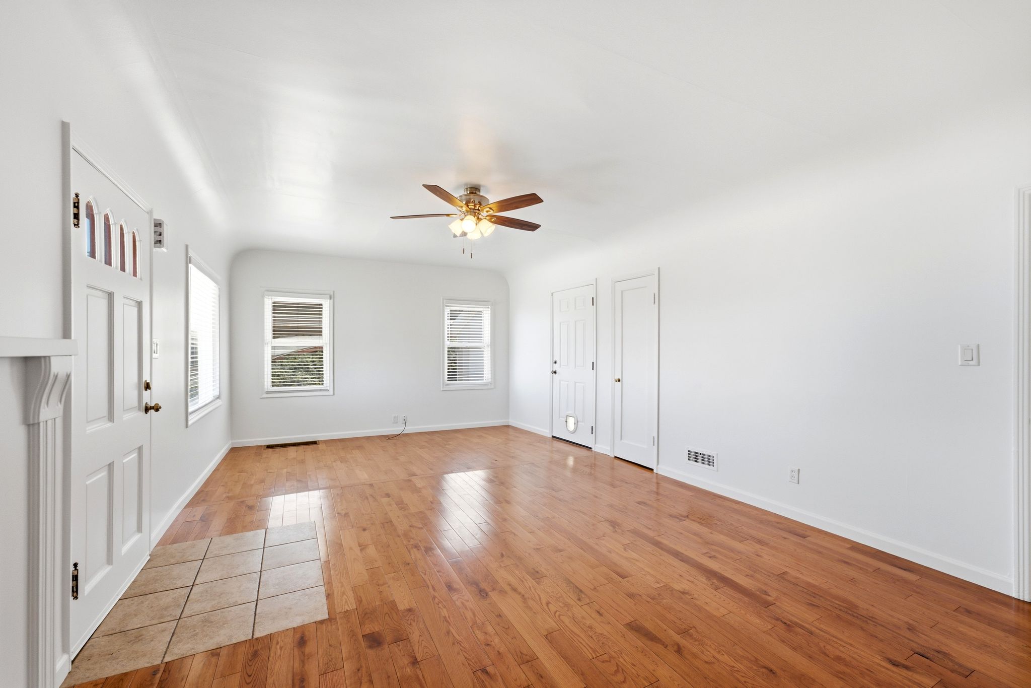 Spacious interior featuring wood-finish flooring, white walls, and a ceiling fan with integrated lighting