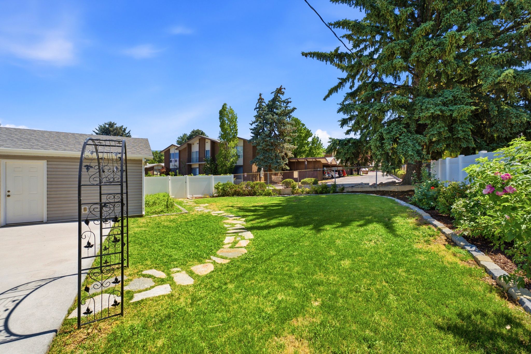 Expansive green lawn with a flagstone pathway, surrounded by mature landscaping and a white privacy fence