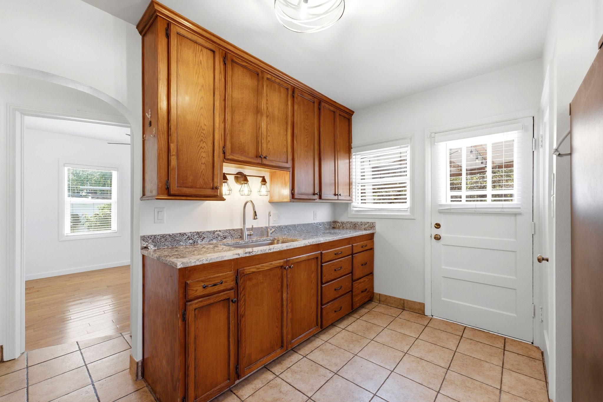 Kitchenette featuring wood cabinetry, undermount sink with a gooseneck faucet, light-toned stone countertop, and tile flooring