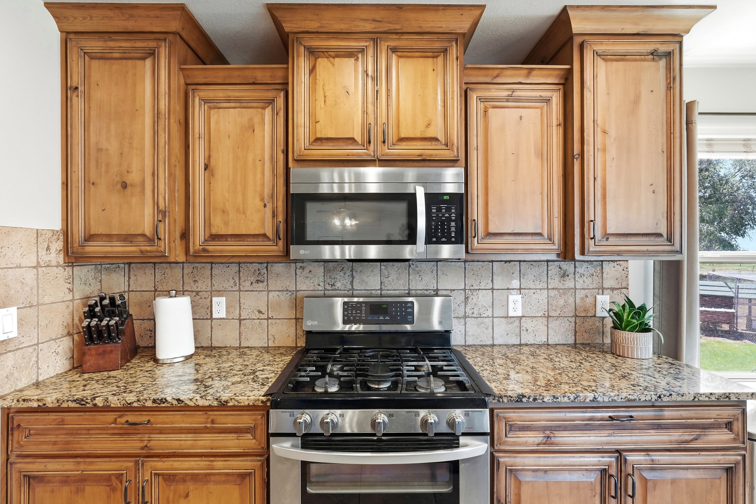 Kitchen featuring wood cabinetry, stainless steel range with gas cooktop, stainless steel microwave, stone tile backsplash, and speckled countertops