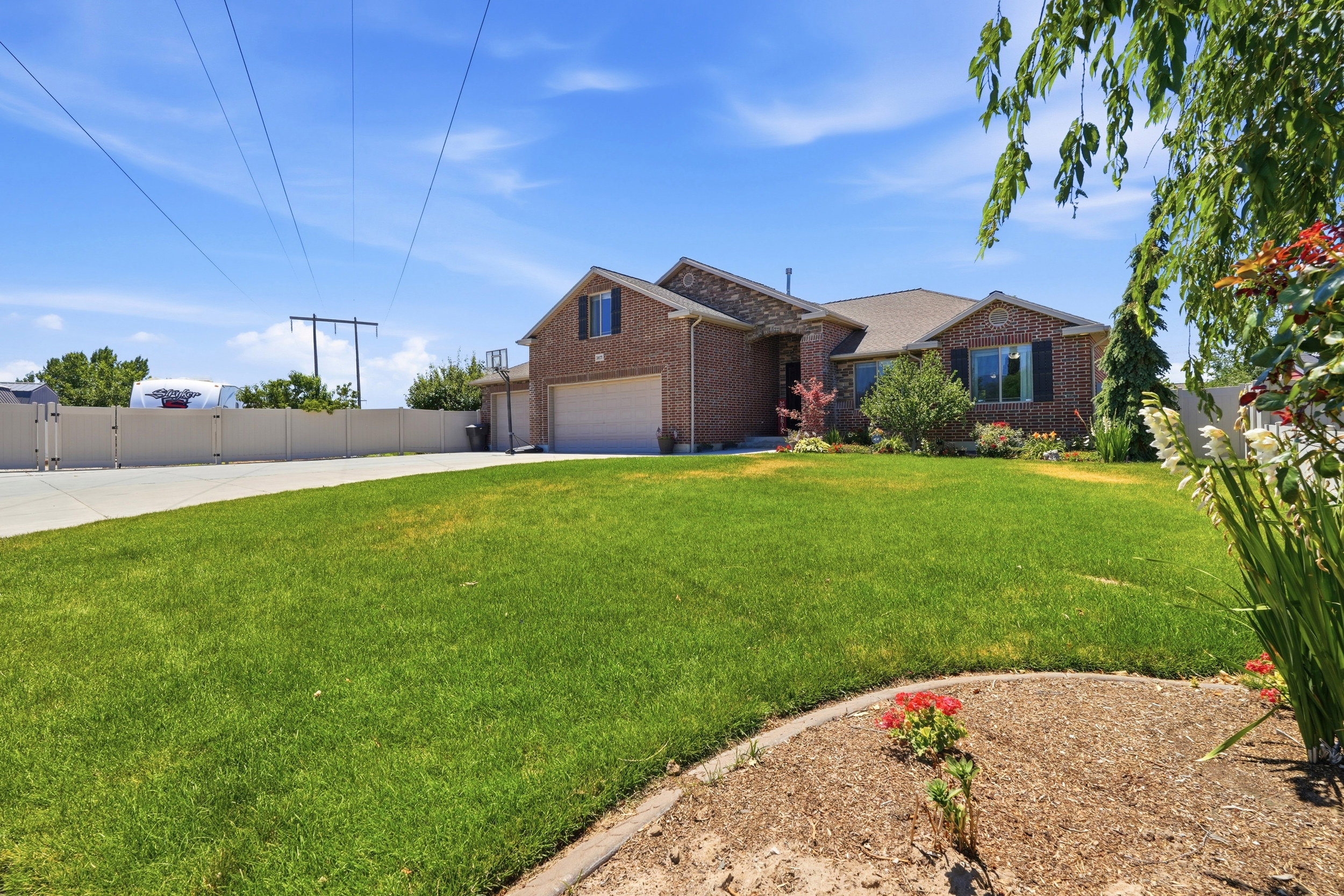 Brick exterior residence featuring a two-car garage, mature landscaping, a paved driveway, and a fenced perimeter