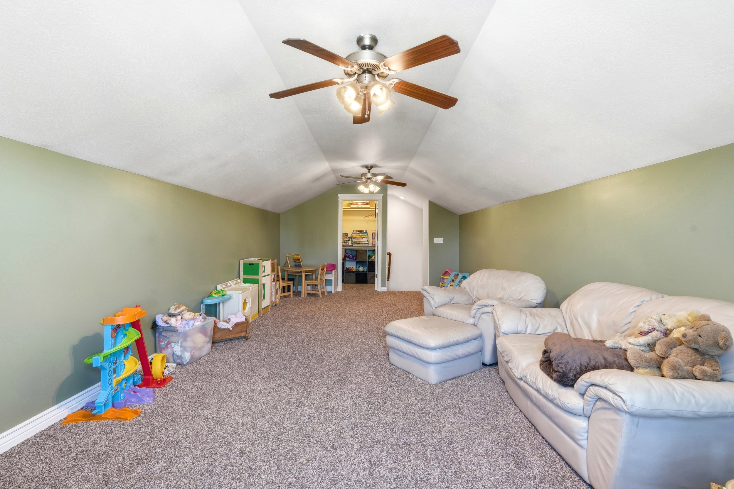 Spacious carpeted room featuring a vaulted ceiling and dual ceiling fans with integrated lighting, offering ample overhead illumination