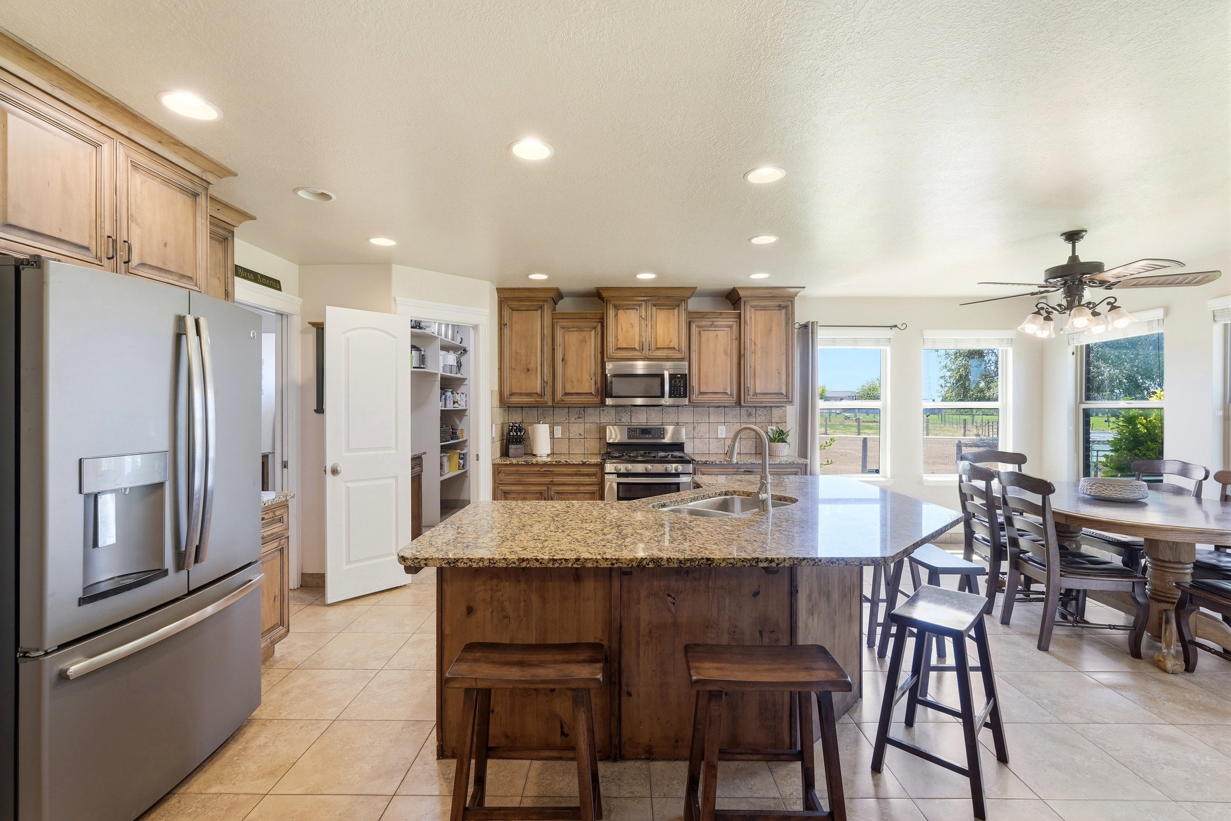 Expansive kitchen featuring a large island with a stone countertop, stainless steel appliances, wood cabinetry, and recessed lighting