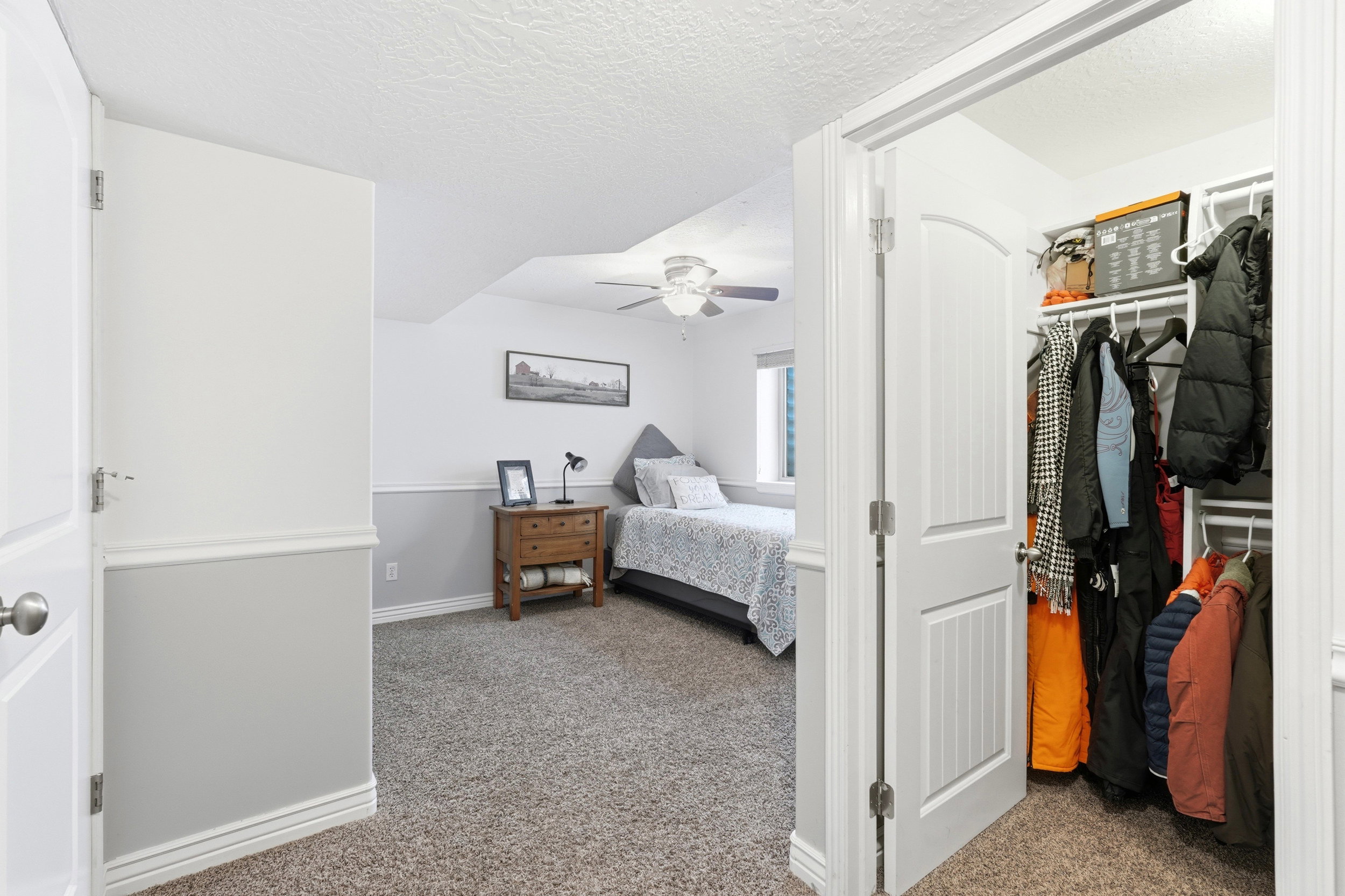 Carpeted room featuring a ceiling fan, window, and a built-in closet with shelving and hanging rods