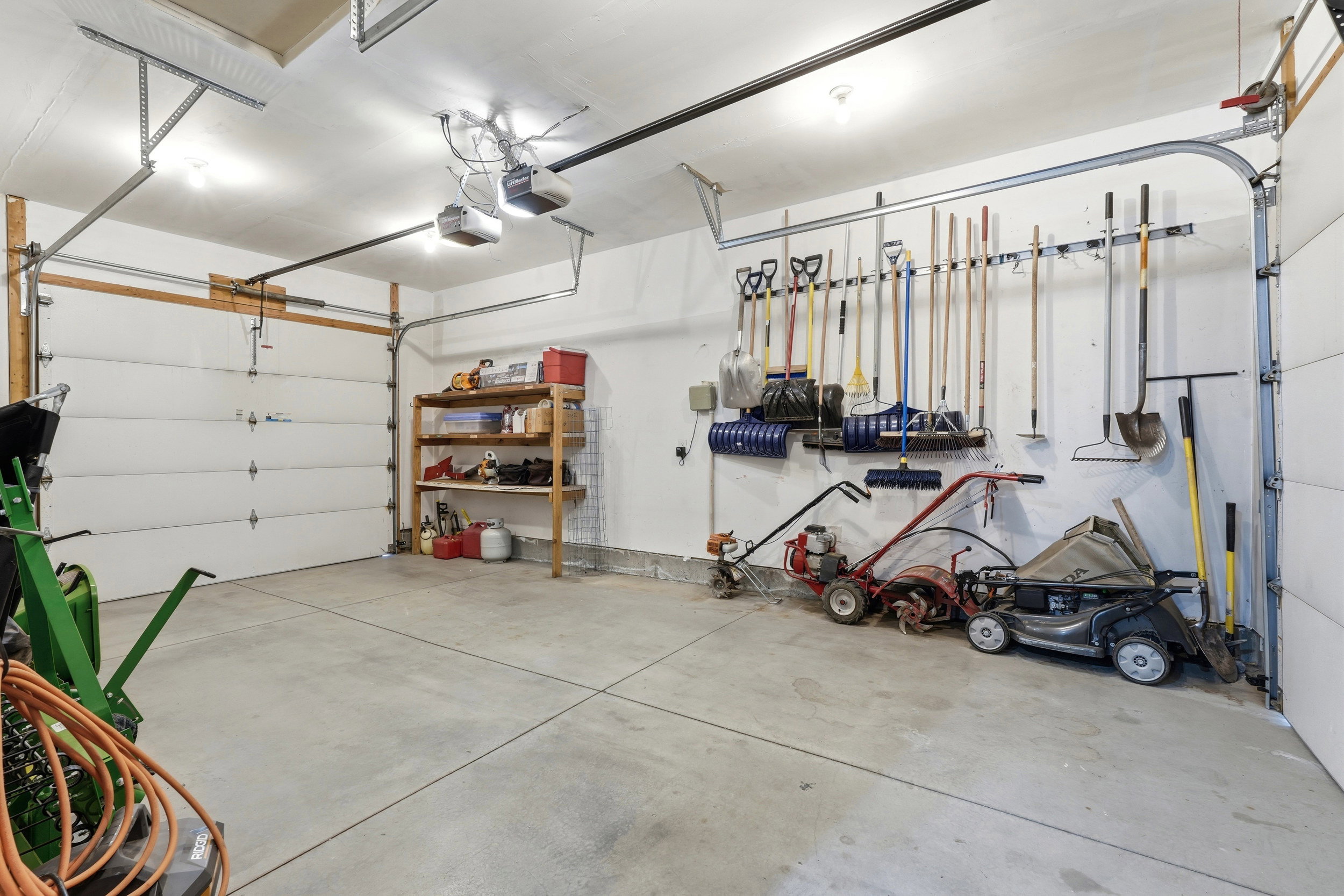 Spacious garage featuring two overhead doors with automatic openers, concrete flooring, built-in shelving, and wall-mounted storage racks