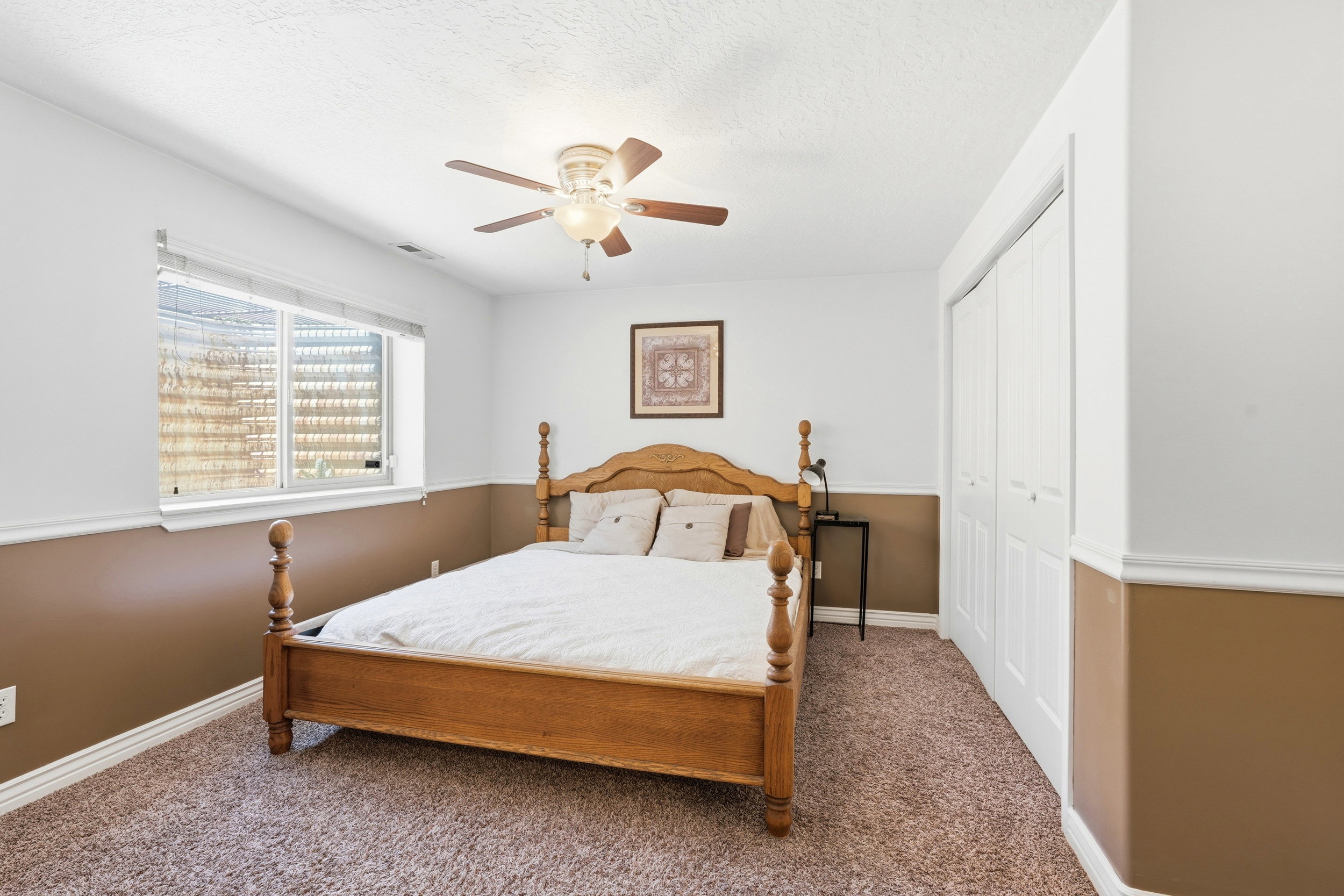 Carpeted room featuring a ceiling fan with integrated lighting, a window with blinds, bi-fold closet doors, and two-tone painted walls with chair rail molding