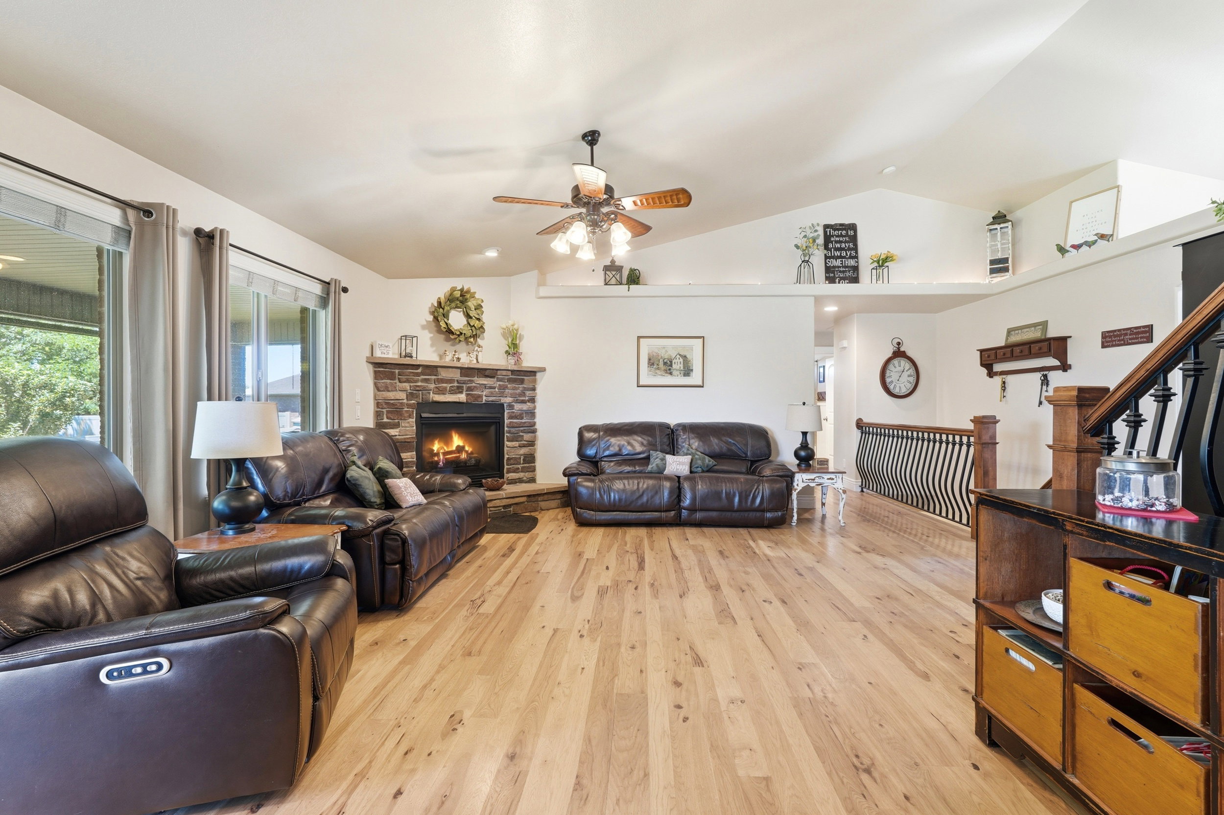 Spacious living area featuring vaulted ceilings, wood-finish flooring, and a stone-faced fireplace