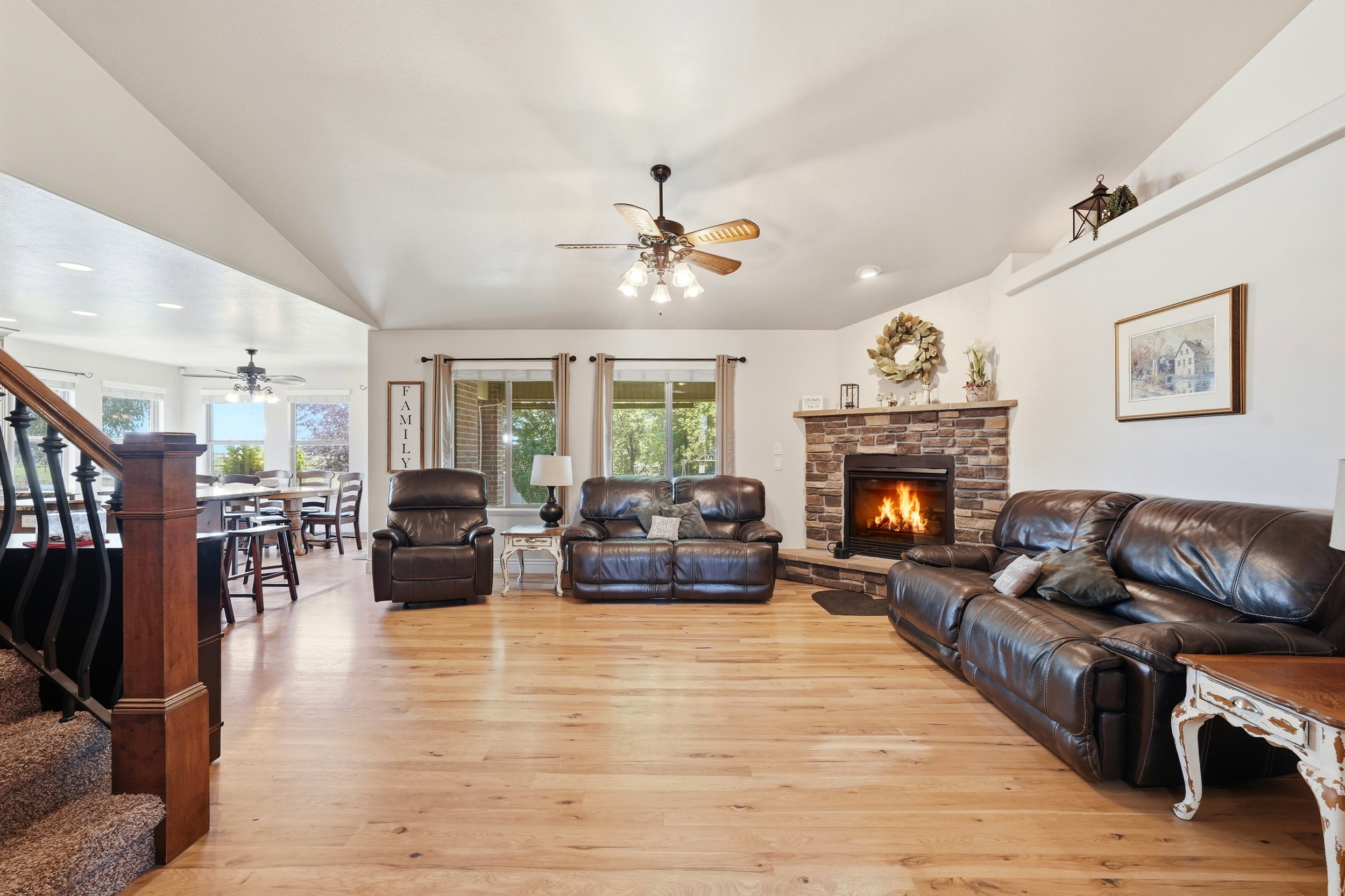Spacious living area featuring light wood-finish flooring, a stone fireplace with a hearth, vaulted ceilings, and recessed lighting