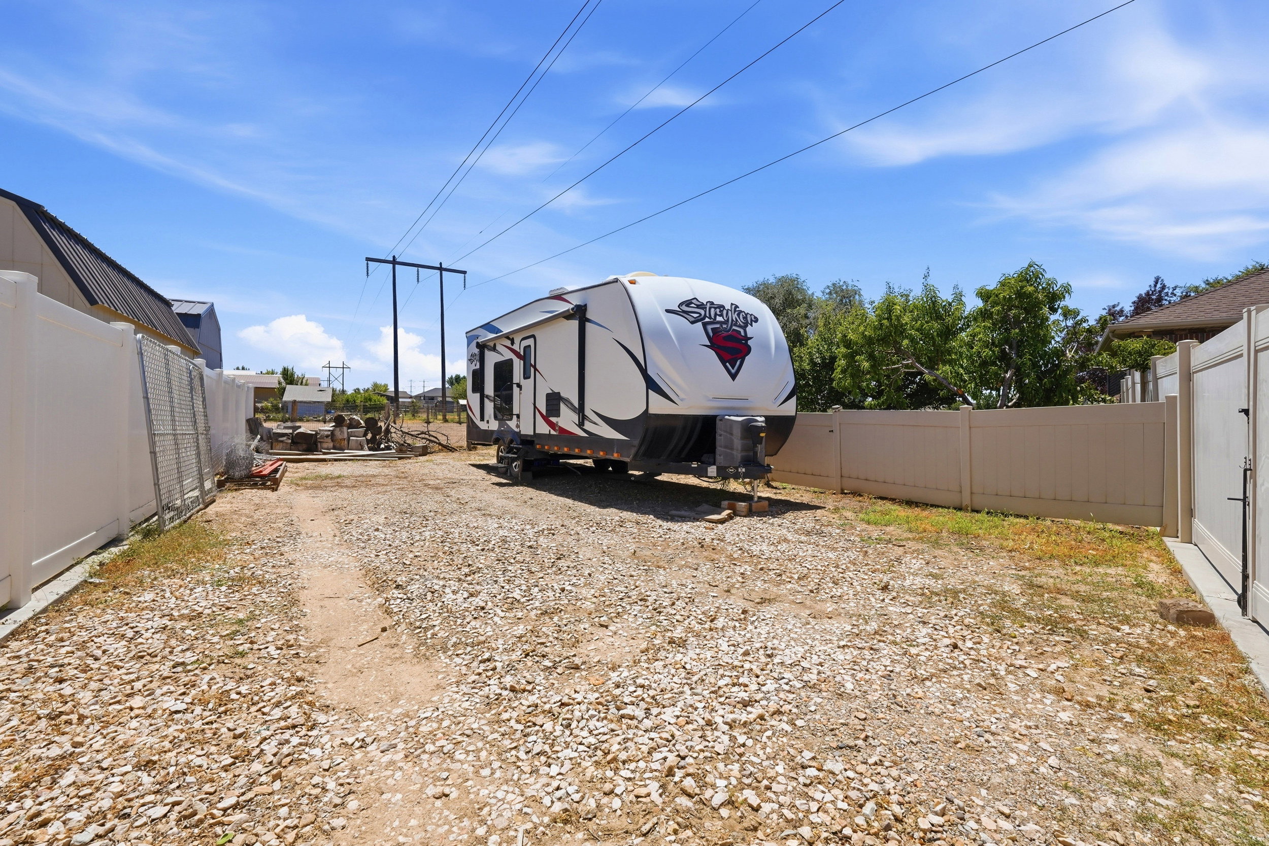 Gravel parking area featuring a white vinyl privacy fence and a rear access gate