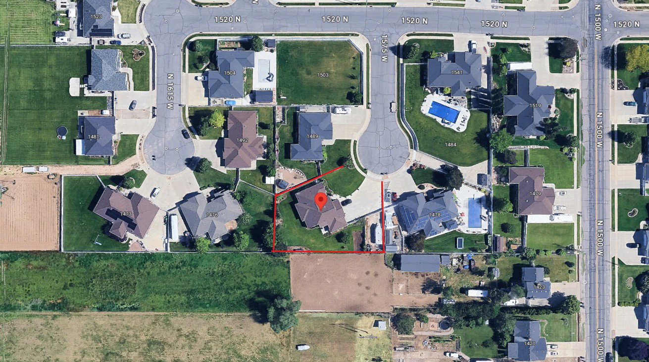 Aerial perspective showcasing a residential property with a dark-toned roof and an expansive rear yard, bordered by open fields