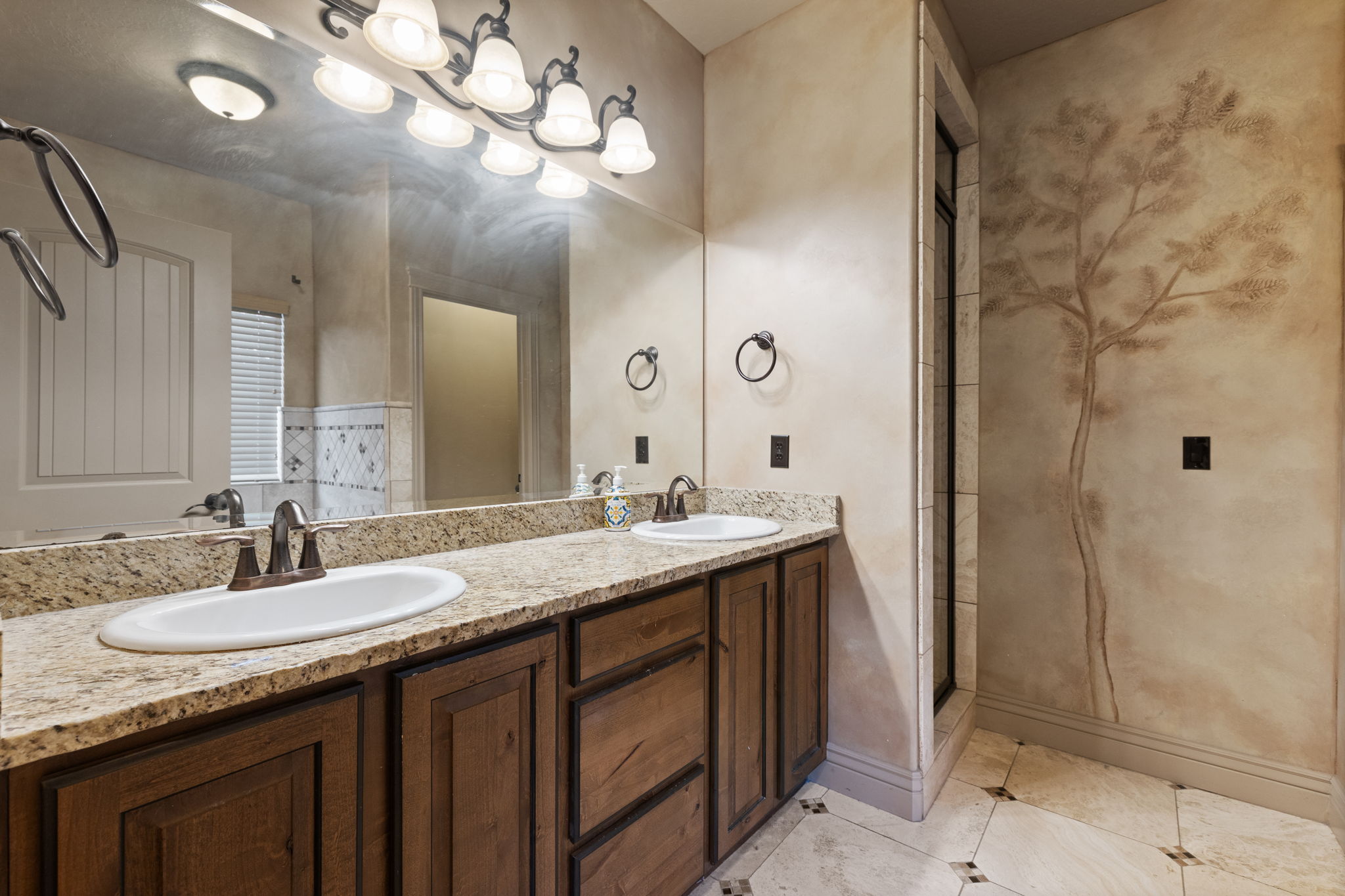 Double vanity with granite countertop, wood-finish cabinetry, and a framed mirror
