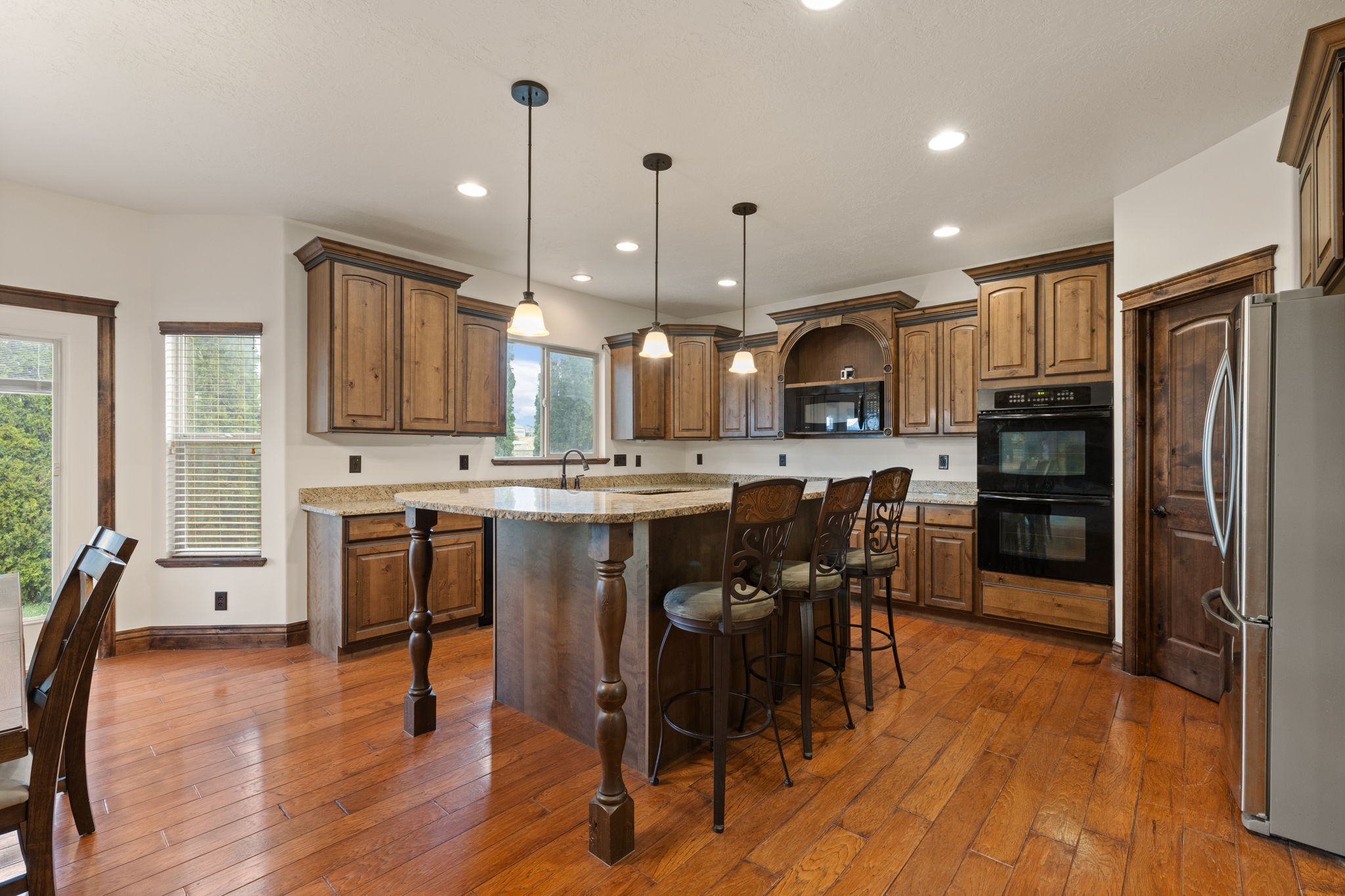 Open-concept kitchen featuring wood-finish flooring, an island with seating, granite countertops, wood cabinetry, and stainless steel appliances