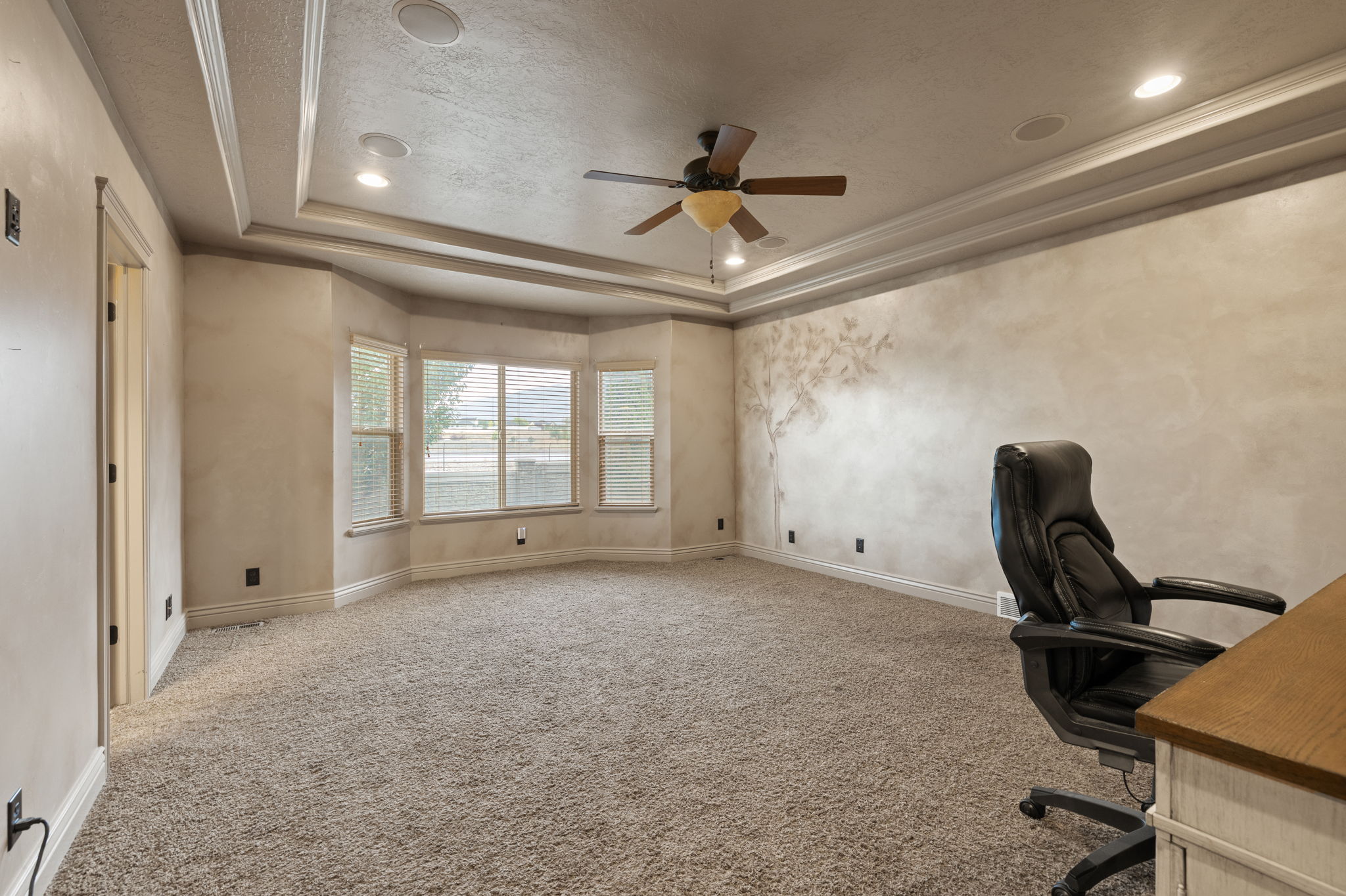 Room featuring a bay window with blinds, tray ceiling with recessed lighting and ceiling fan, textured wall finish, and neutral-toned carpeting