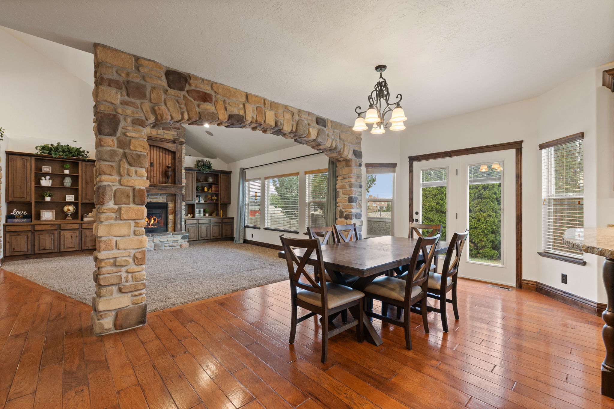 Open-concept living area with wood-finish flooring, a stone-clad archway, and a vaulted ceiling