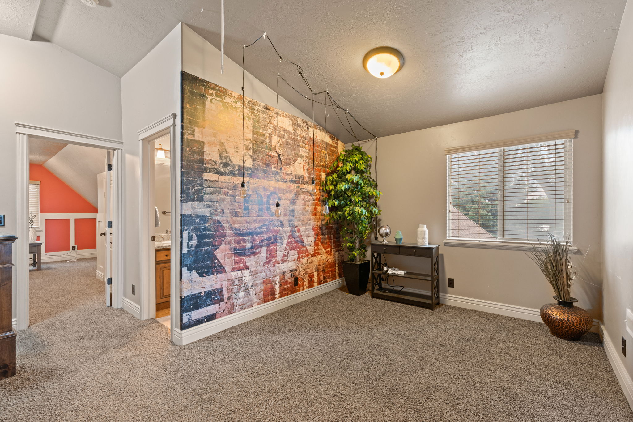 Carpeted room featuring a distinctive accent wall with a distressed brick-style graphic, a window with horizontal blinds, and a built-in light fixture