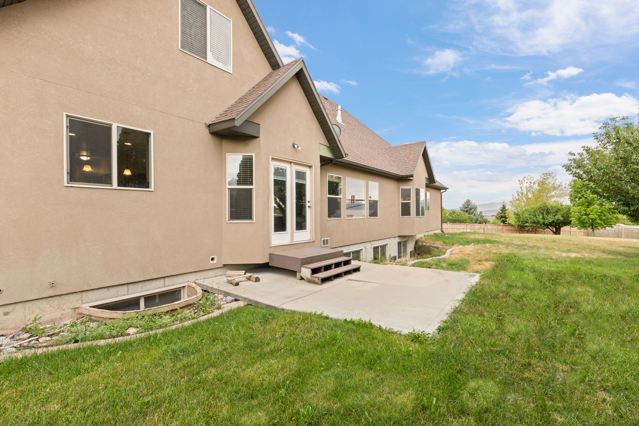 Rear exterior featuring stucco siding, a concrete patio, and a tiered deck with steps