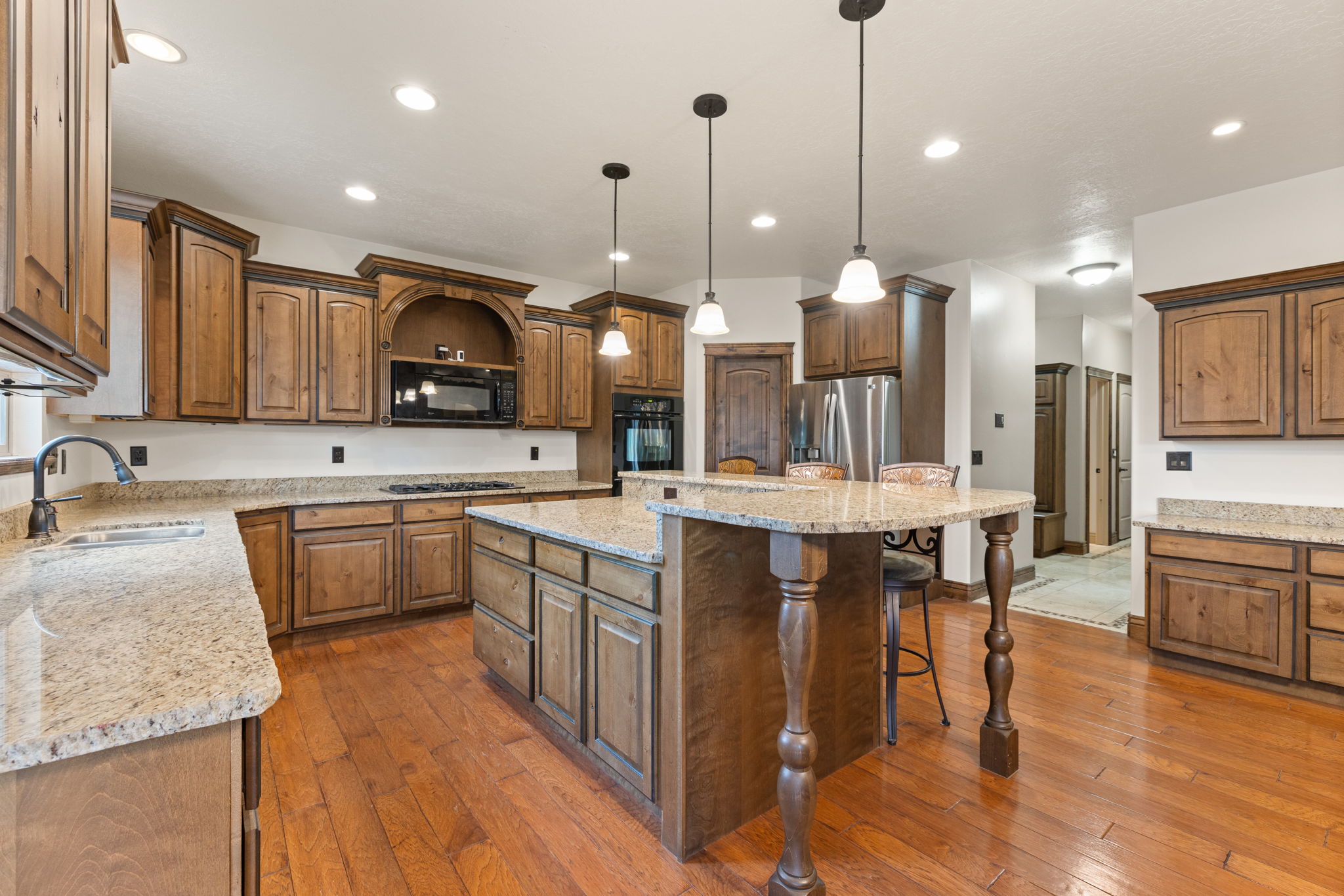 Kitchen featuring wood-finish flooring, abundant cabinetry, stone countertops, a central island with seating, and stainless steel appliances