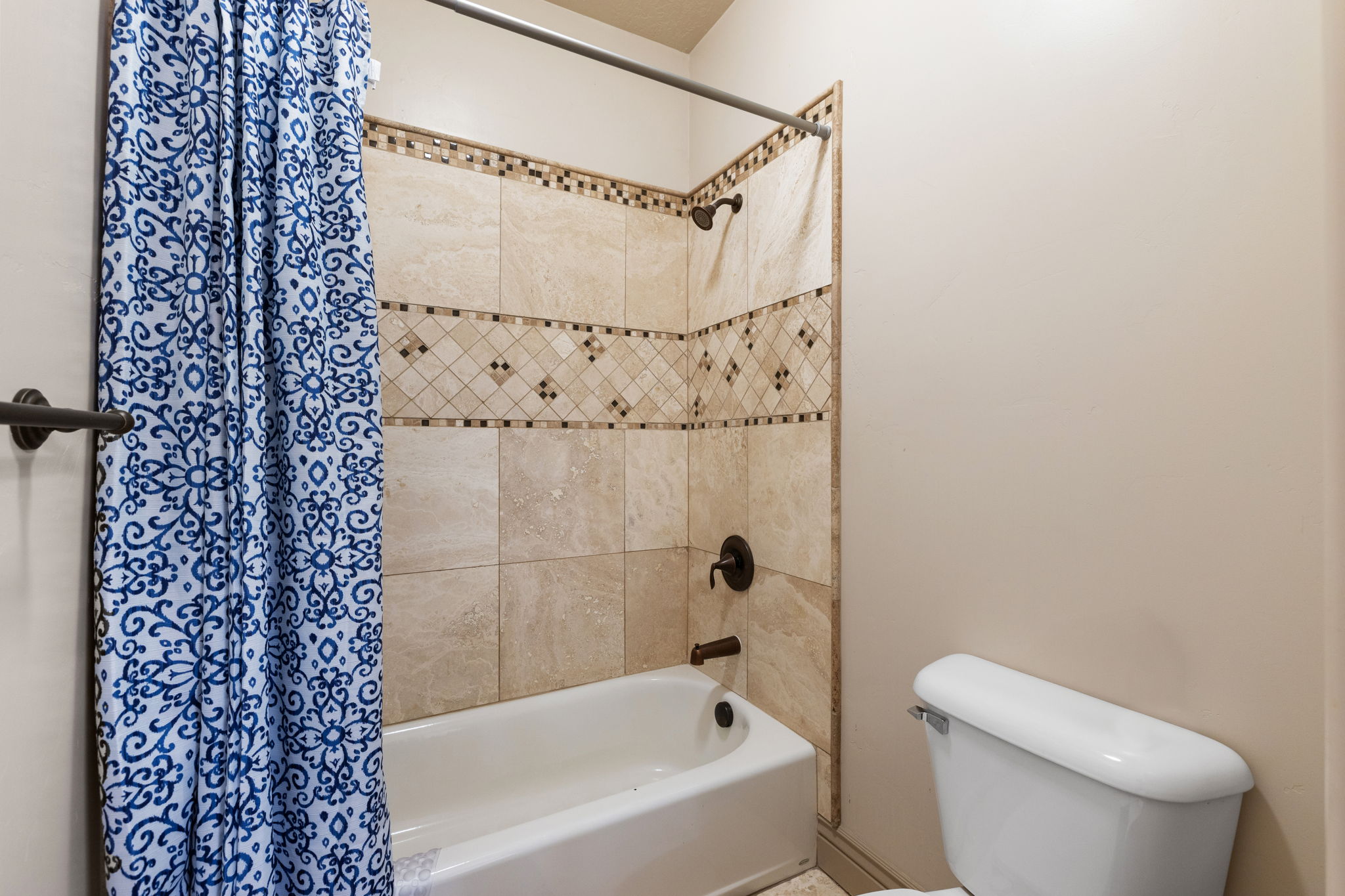 Bathtub shower combination with tiled surround featuring decorative mosaic accents